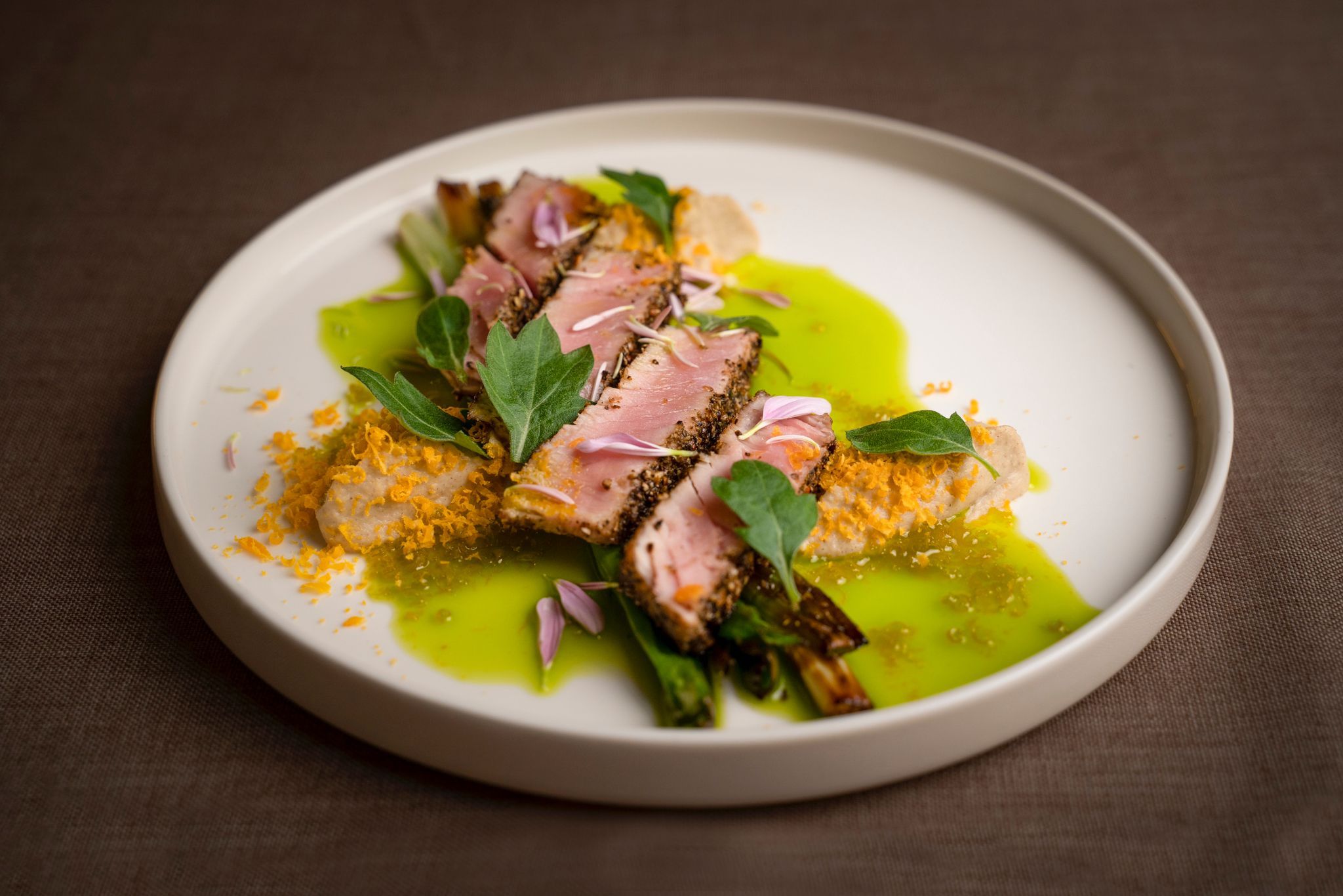 An artfully prepared dish with meat, green sauce and edible flowers on a white plate.