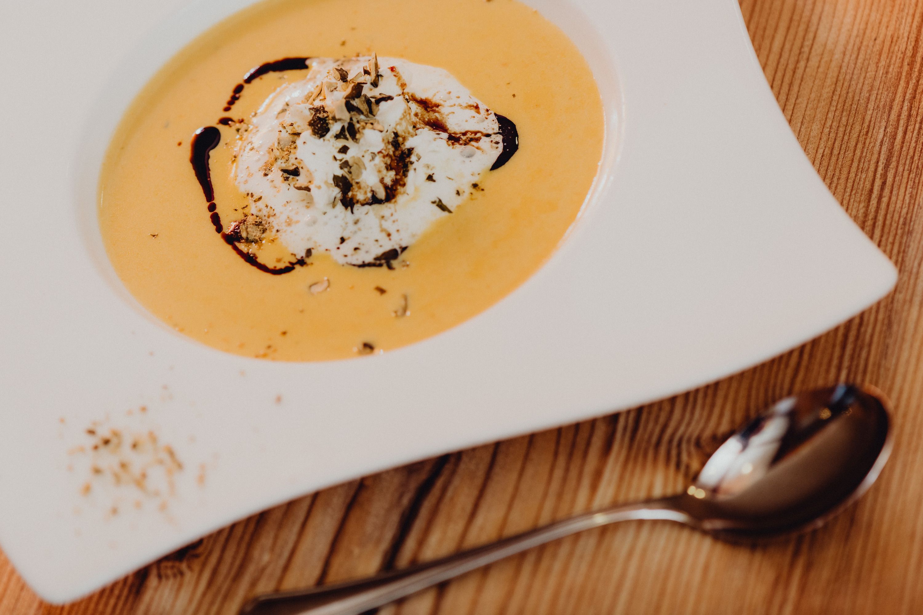 Pumpkin soup with cream and pumpkin seed oil in a white plate on a wooden table.