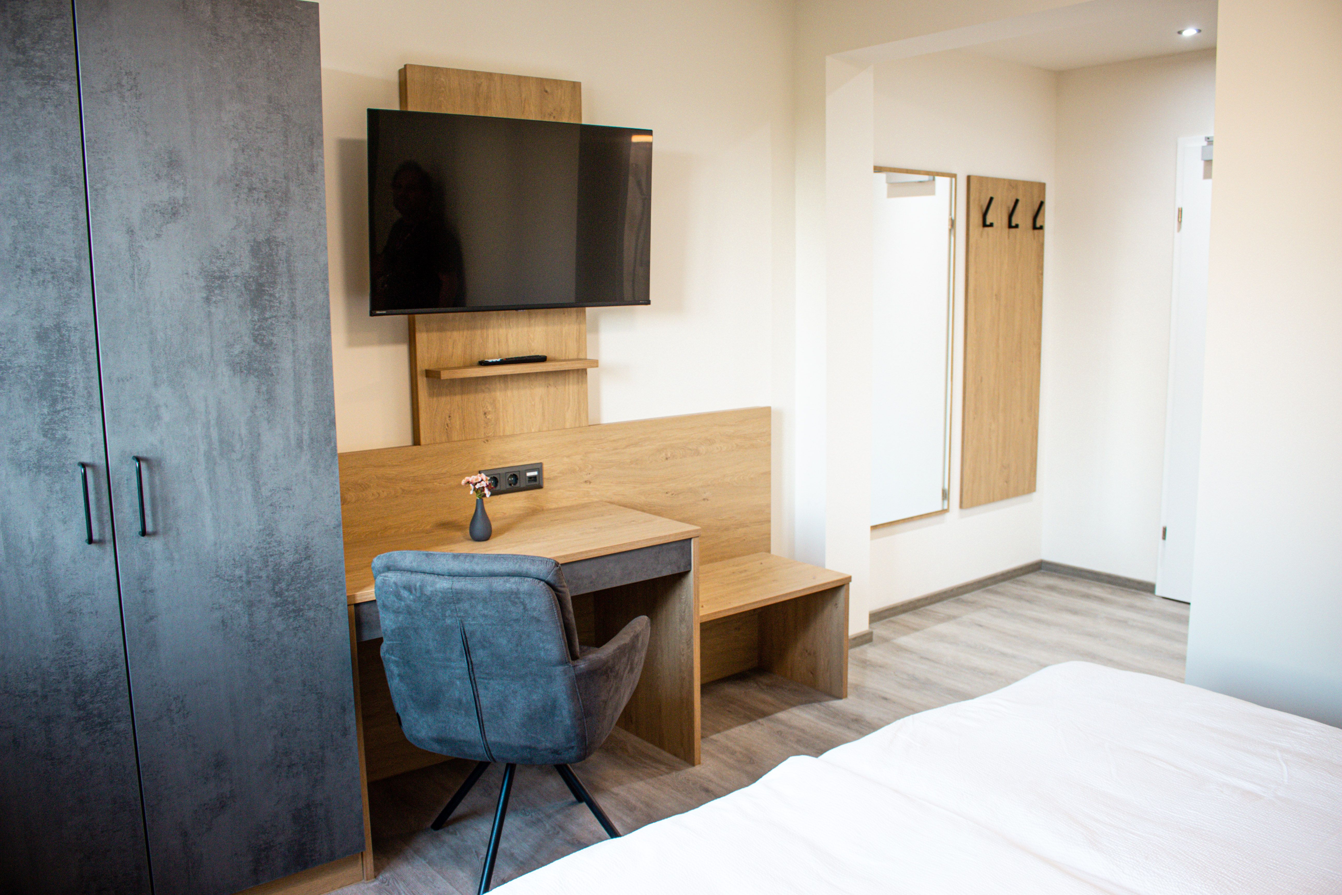 Modernly furnished hotel room with desk, TV, closet and mirror.