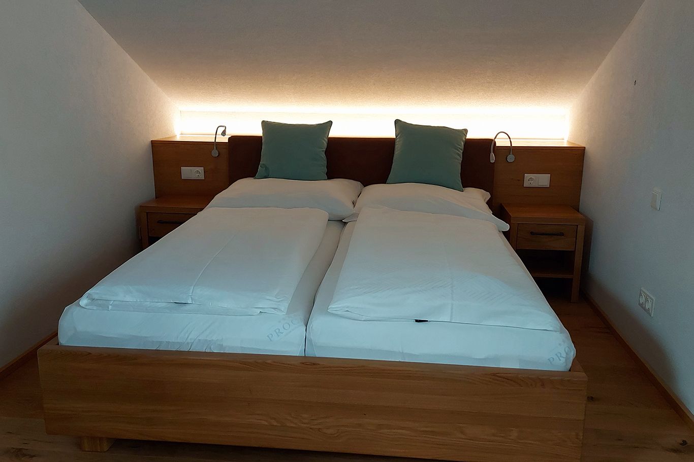 A double bed in a room with a sloping ceiling, two pillows and bedside tables.