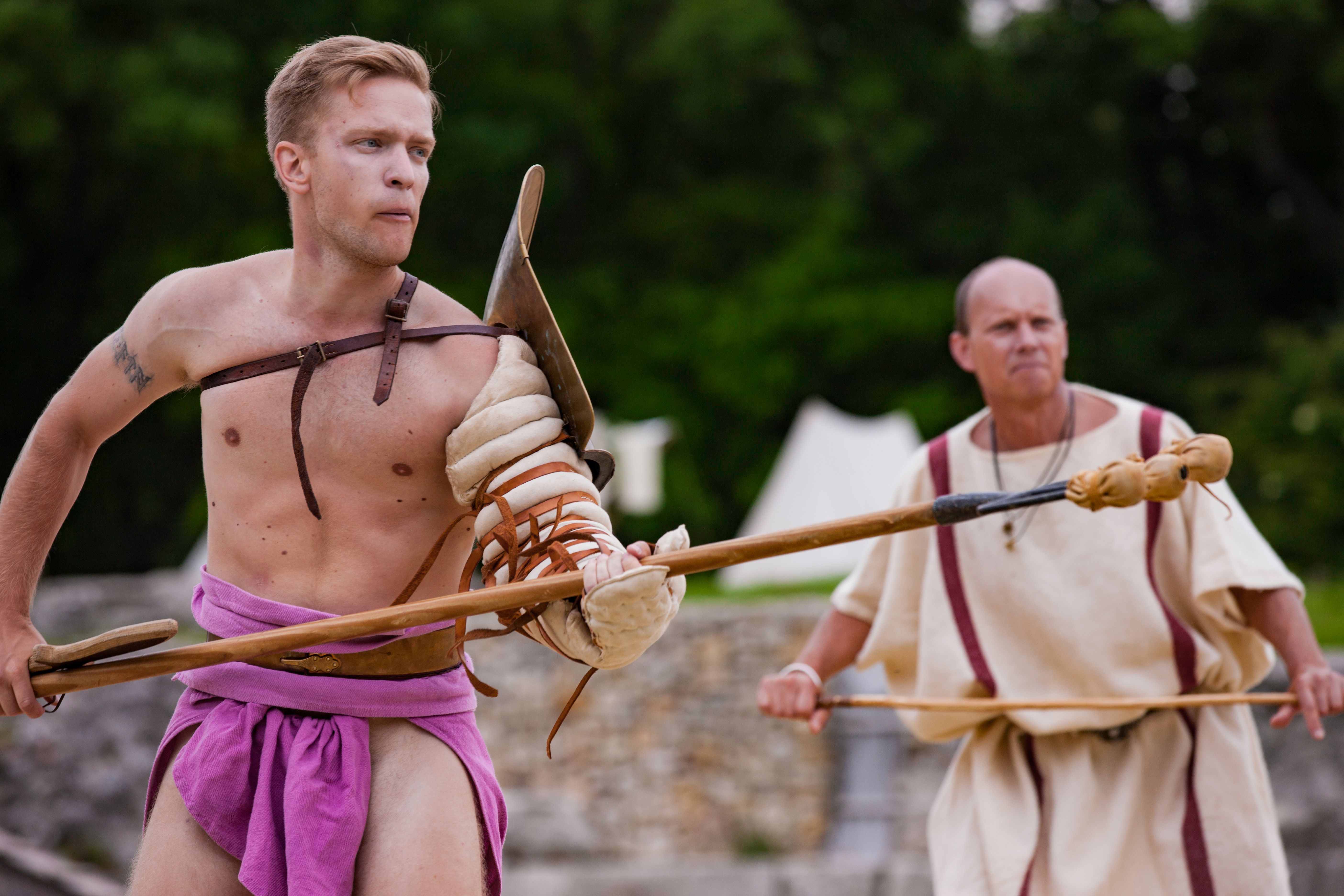 Two men in gladiator costumes with spears outdoors.