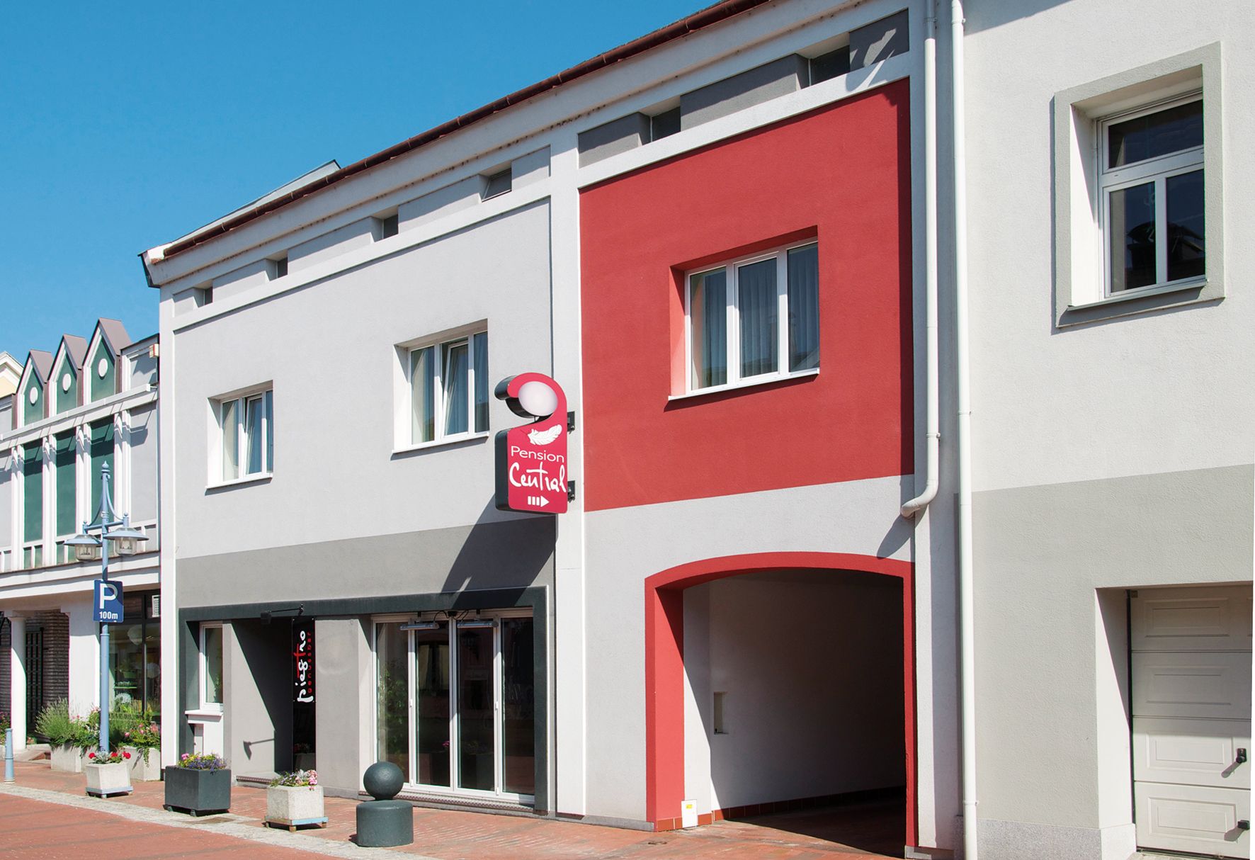 Facade of the Pension Central with gray and red walls, a sign and windows.