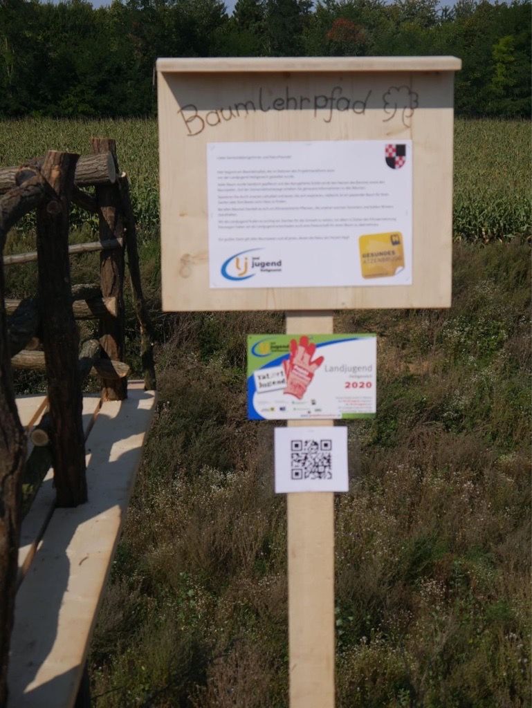 Wooden sign with information about the Atzenbrugg educational tree trail, surrounded by nature.