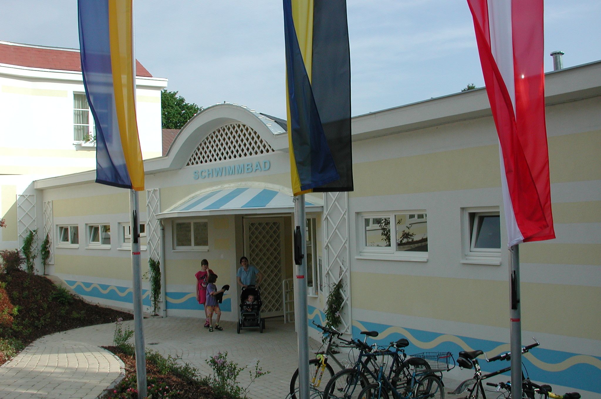 Entrance to a swimming pool with flags and bicycles in front of it.