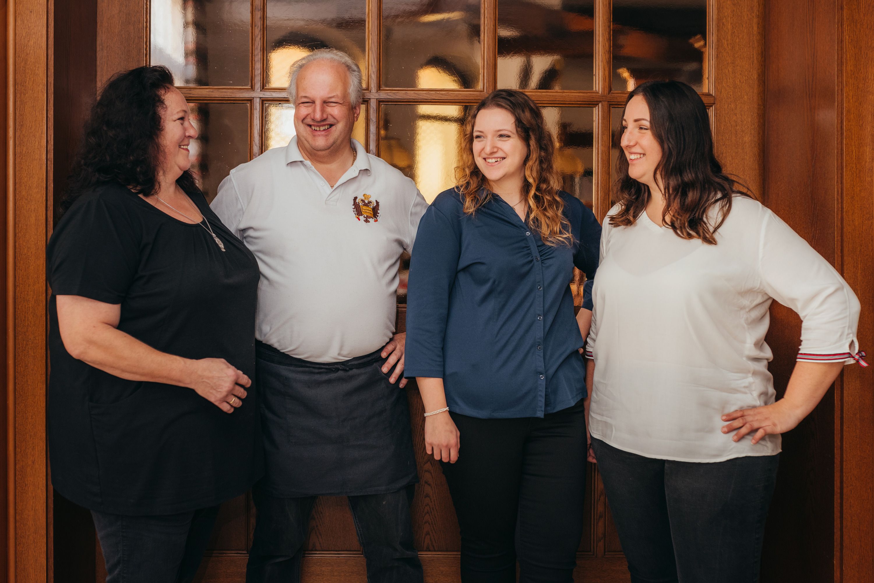 Four people smile in front of a wooden door in an interior room.