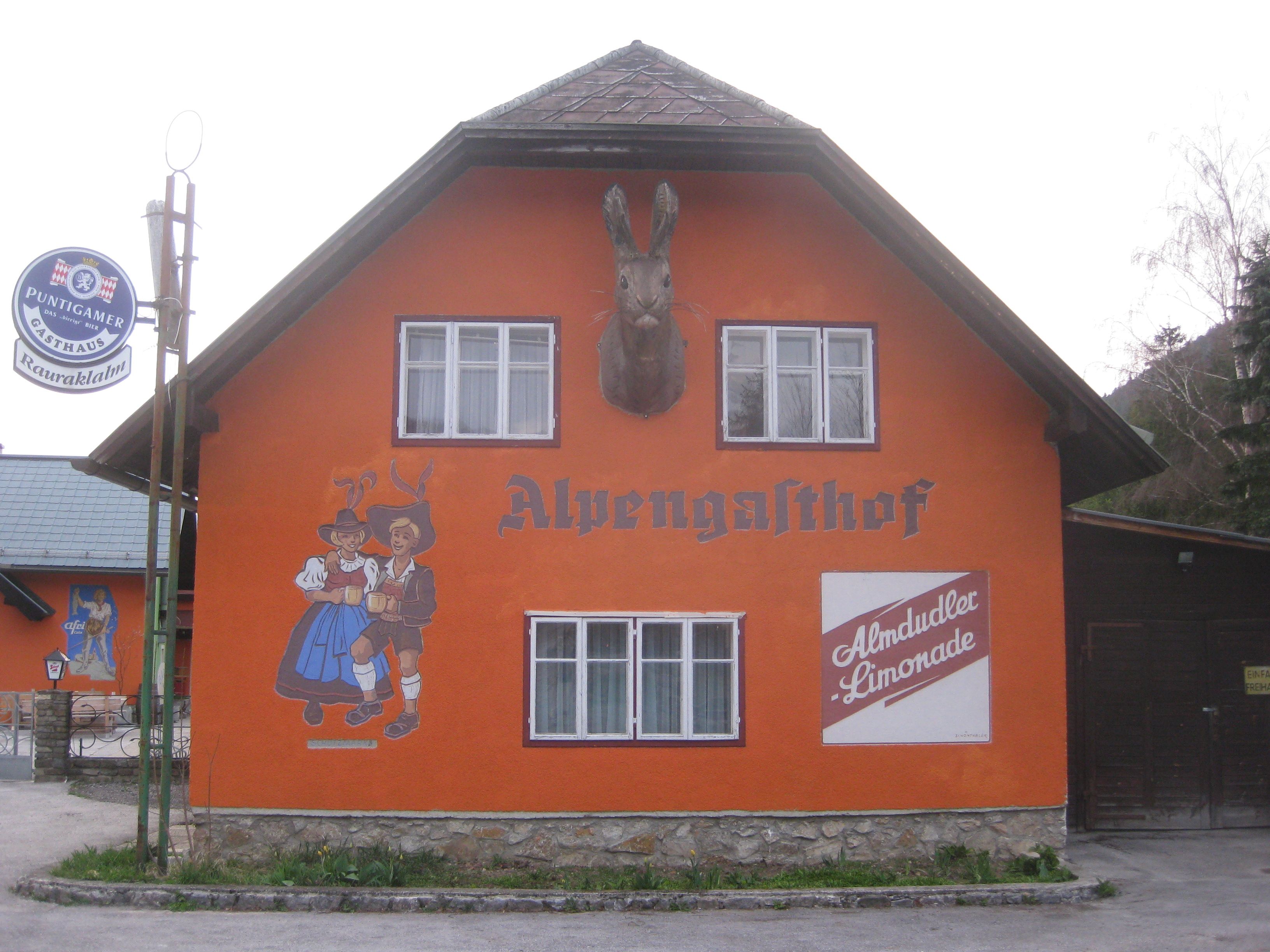 Orange-painted building with the inscription 'Alpengasthof', wall painting of dancing couple and Almdudler advertisement.