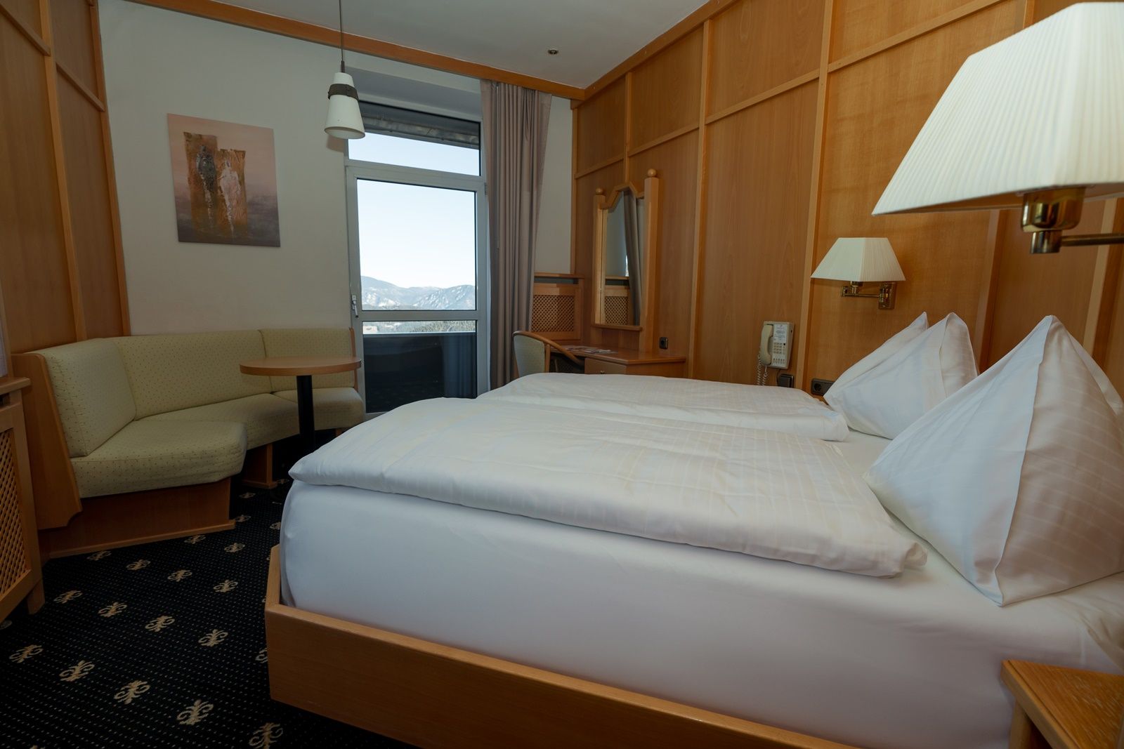 A cozy double room with wooden furniture, a double bed, a seating area and a balcony with mountain views.