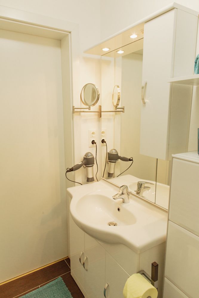 Modern bathroom with washbasin, mirror, hairdryer and white cupboards.