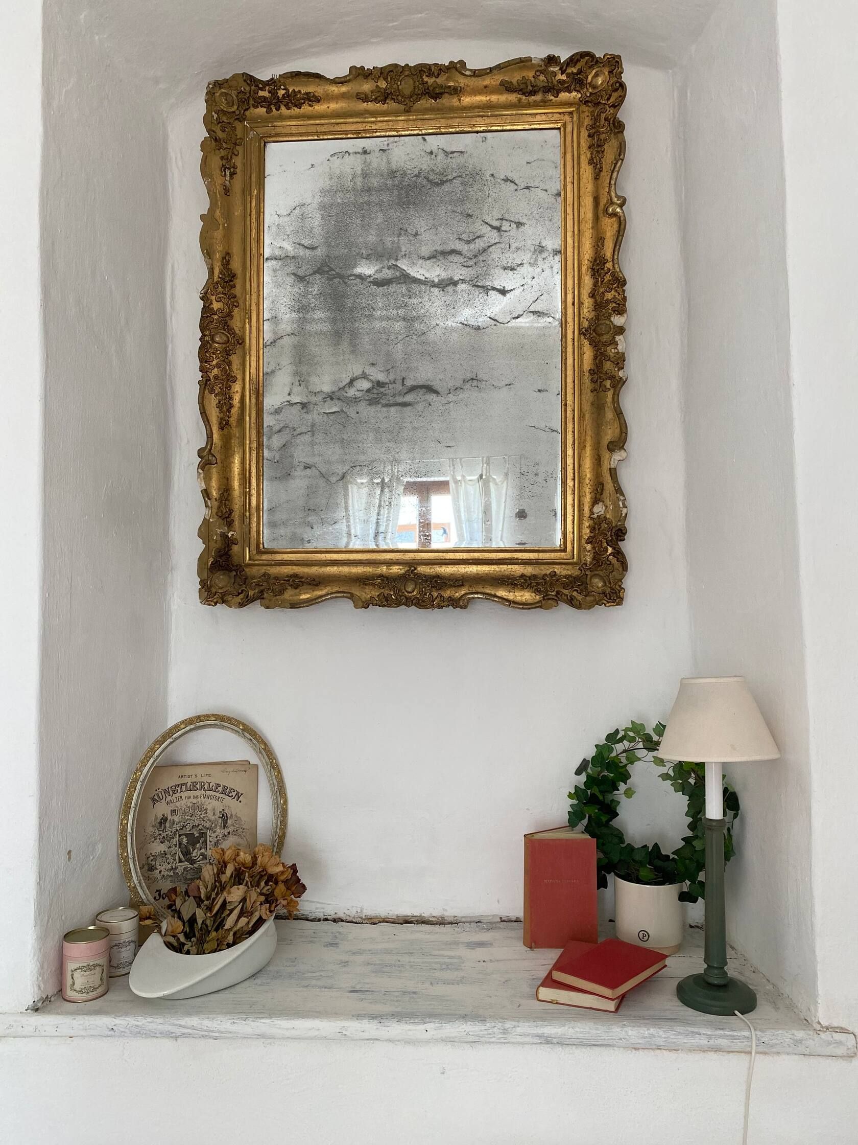 An antique mirror with golden decoration above a windowsill with decoration.
