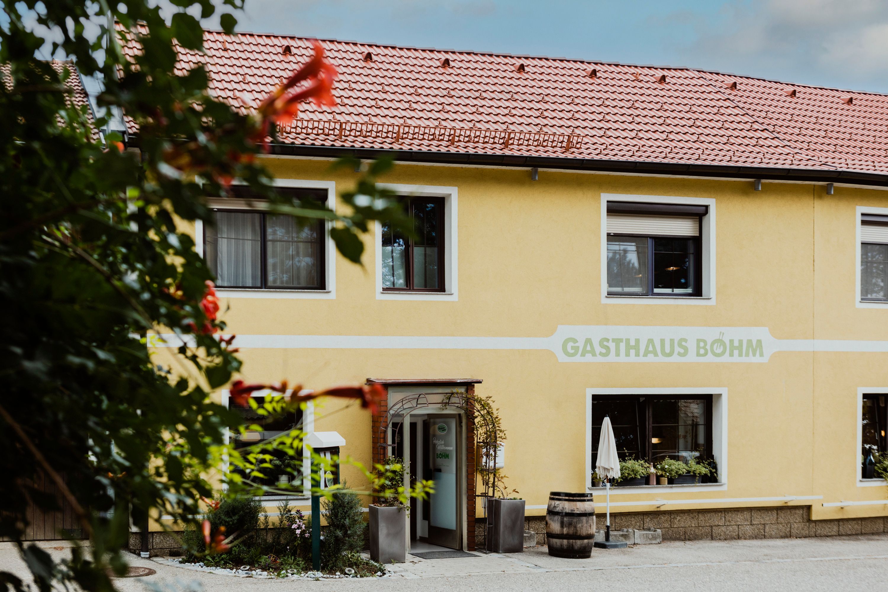 Yellow inn with red roof tiles and plants in front of the entrance.