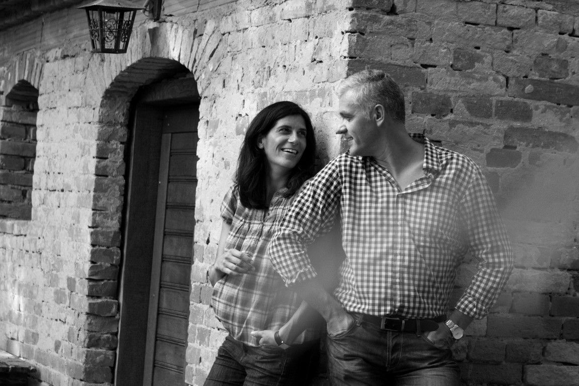 A man and a woman lean against a brick wall, smiling.