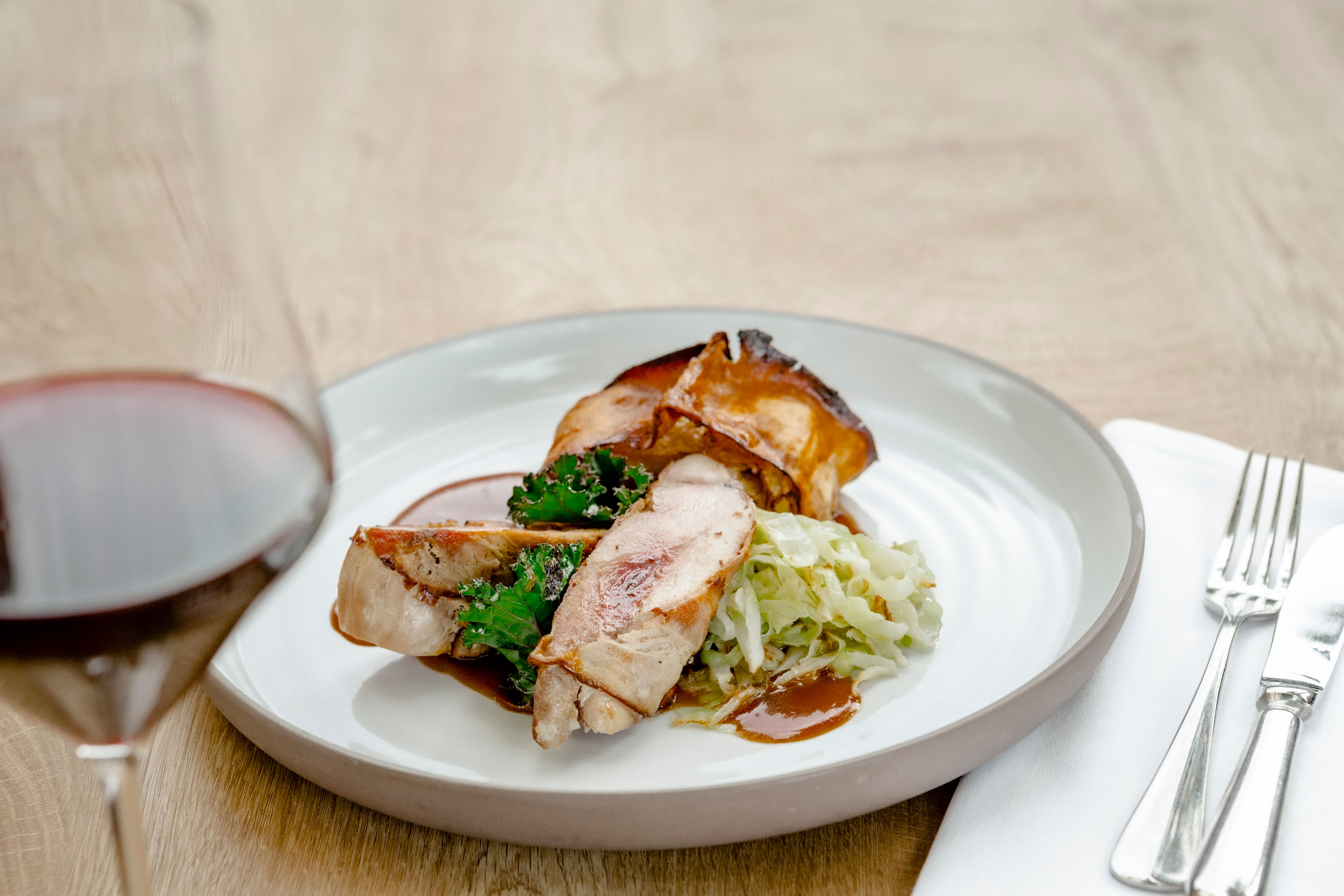 A plate of pheasant breast, kale and cabbage, with a glass of red wine next to it.