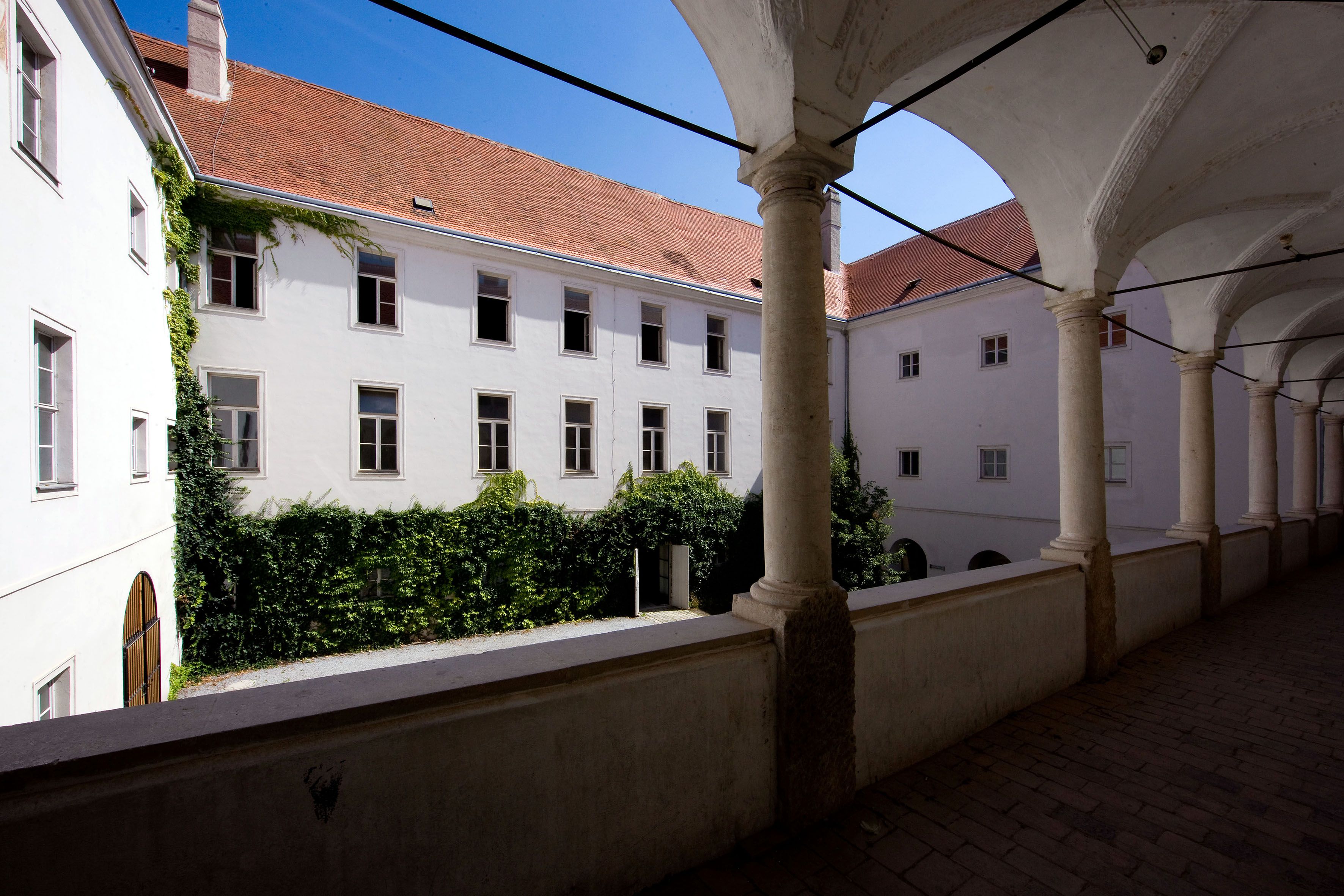 Inner courtyard of a historic building with arcade and ivy-covered walls.