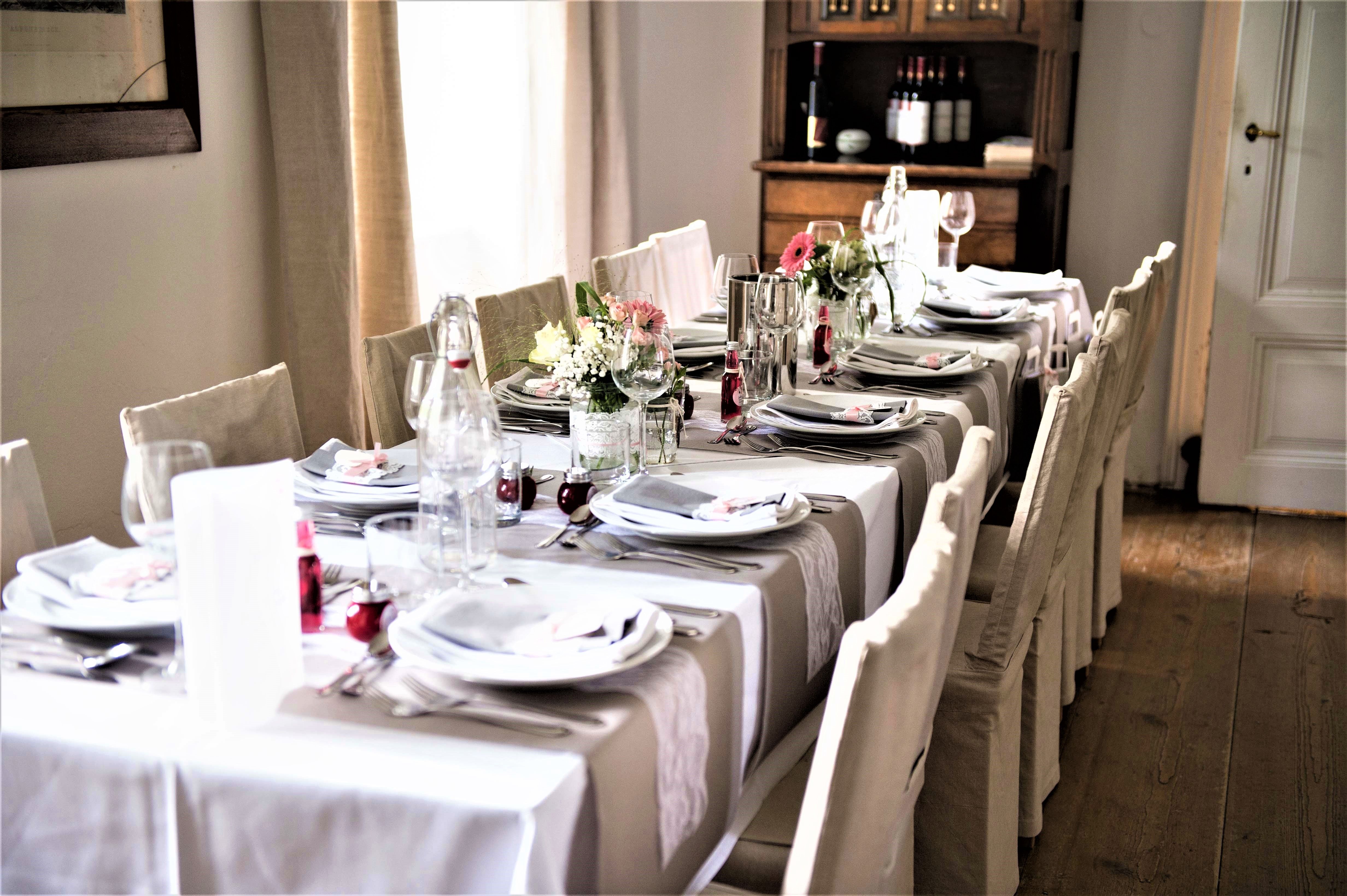 Elegantly laid table with white tablecloths, flower arrangements and crockery in a room with a wooden floor.