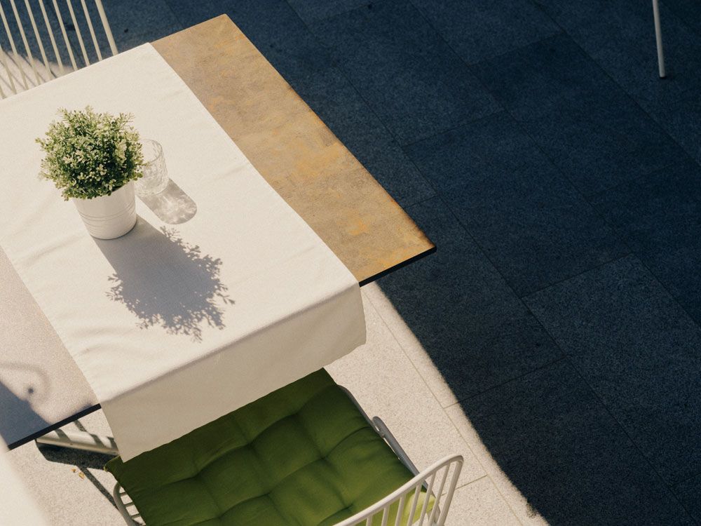 A table with a white tablecloth, potted plant and glass outside.