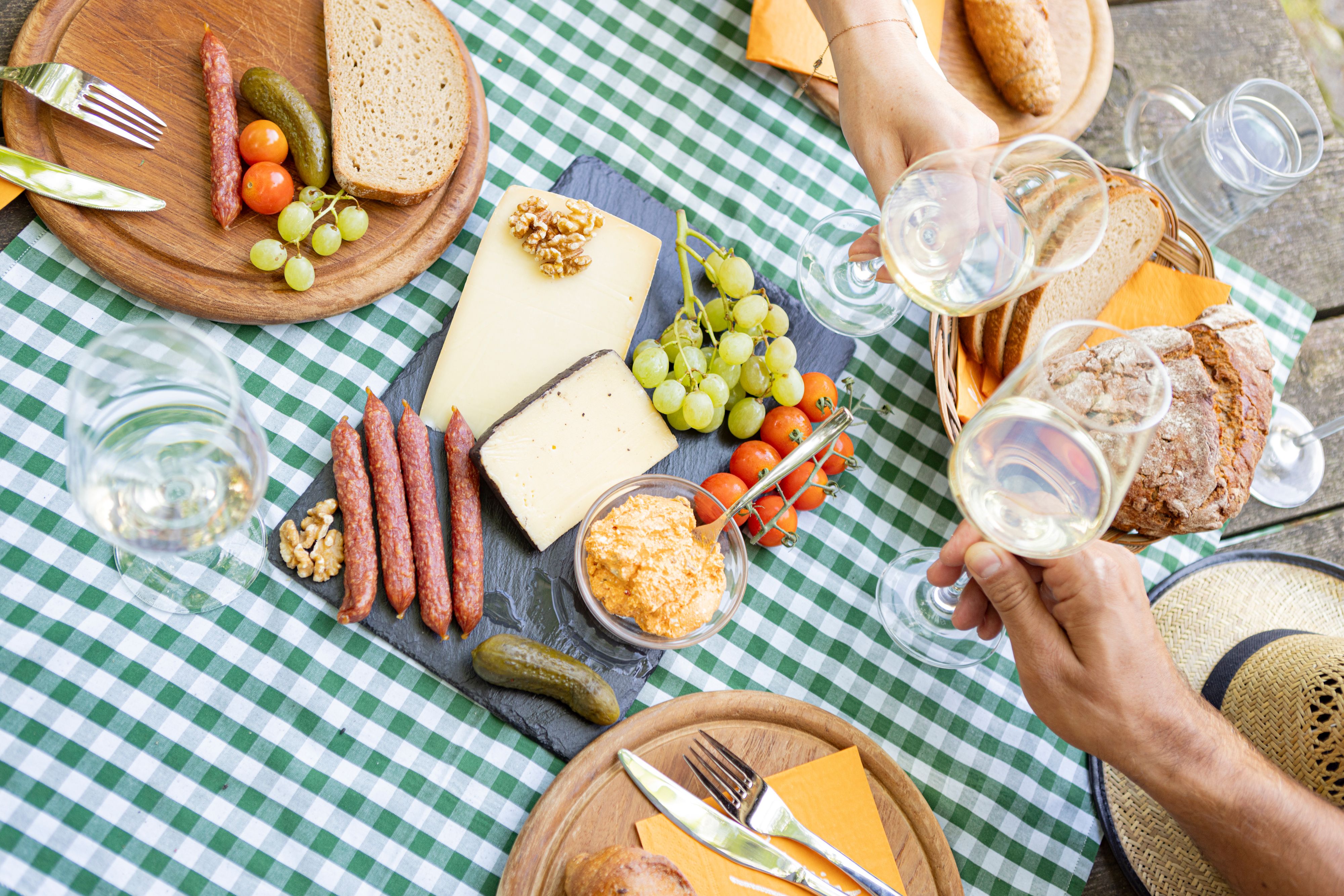 Picnic table with cheese, sausage, bread and wine on a checkered cloth.