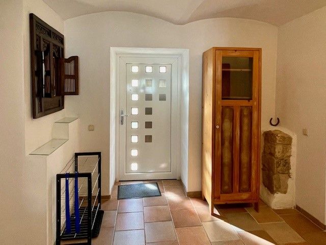 Entrance area with white door, wooden cupboard and tiled floor.