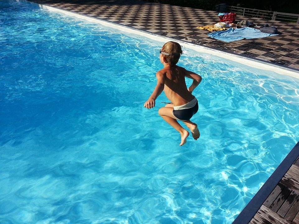 A child jumps into a pool of clear blue water.