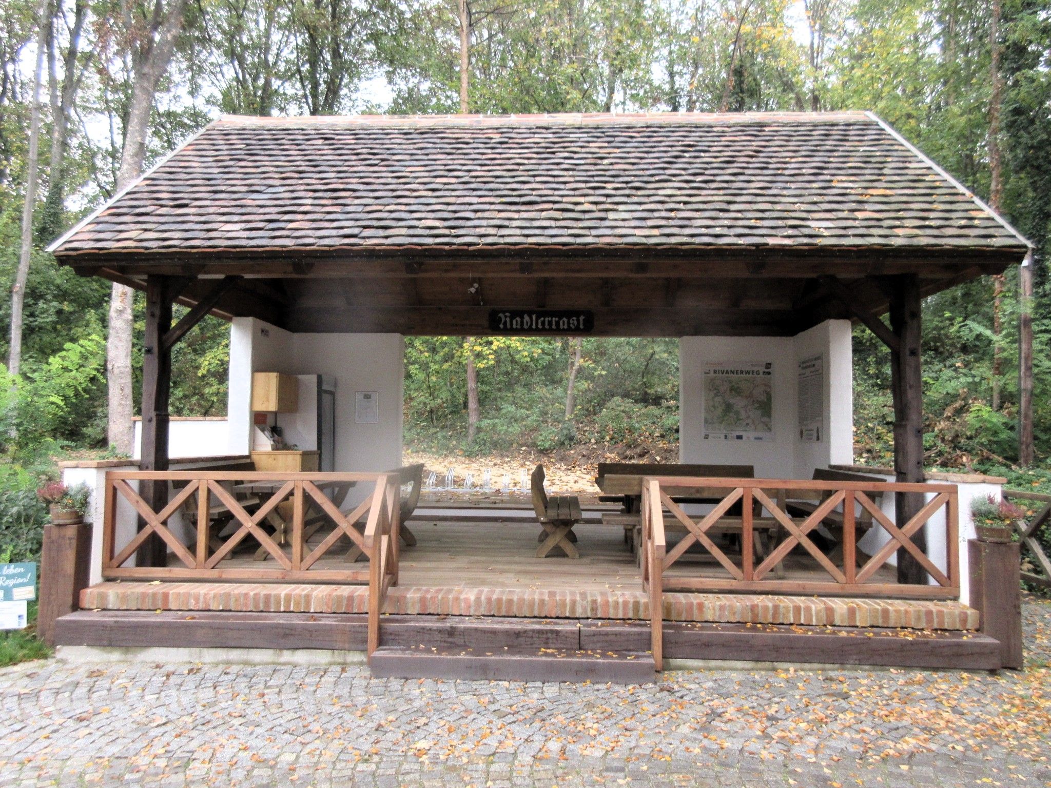 Covered rest station for cyclists in the forest with seating and information signs.