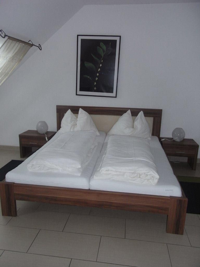 A simply furnished bedroom with a double bed, two bedside tables and a plant picture on the wall.