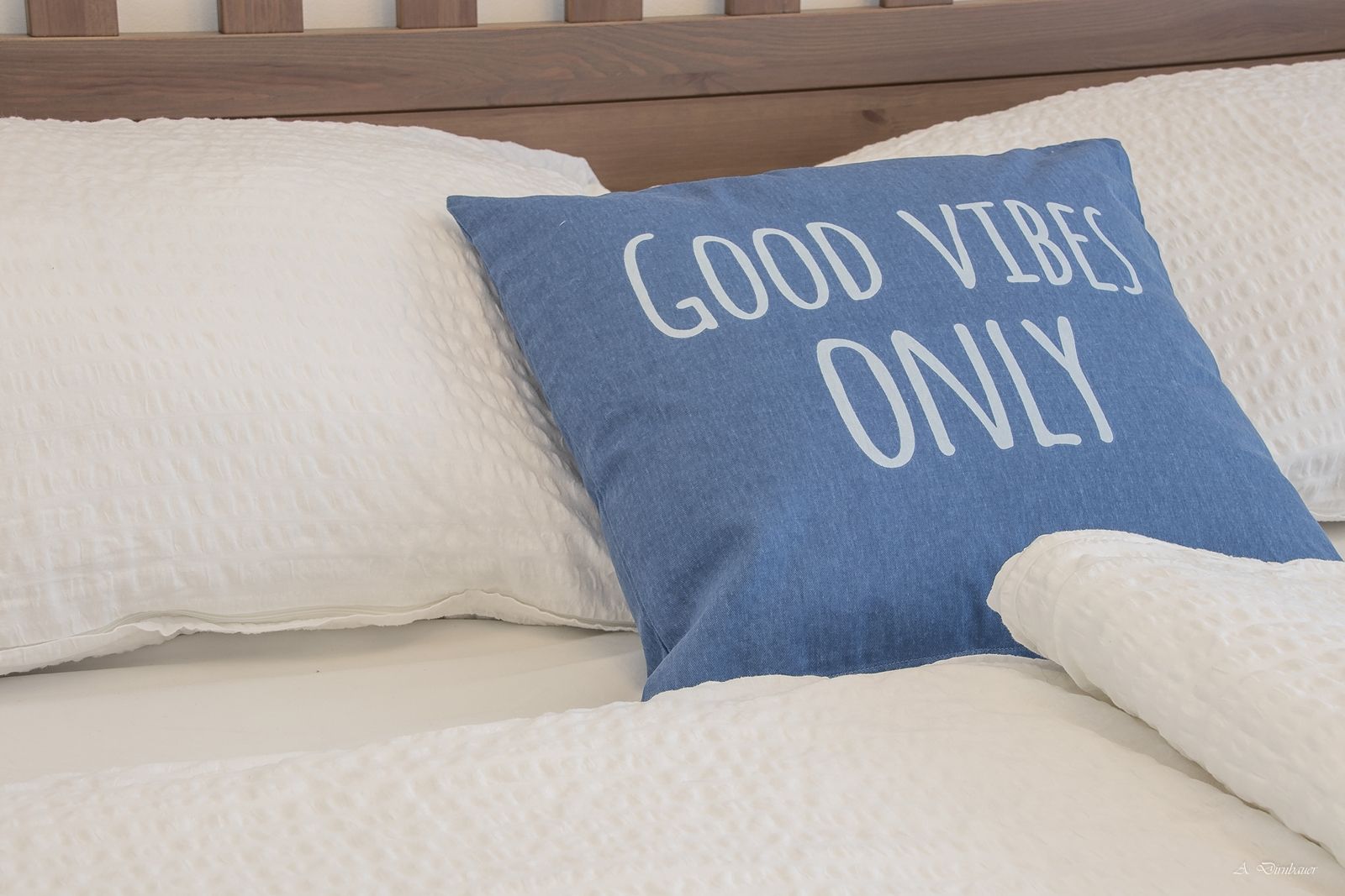 Bed with blue cushion, inscription 'Good Vibes Only'.