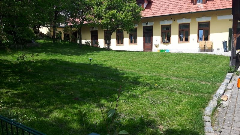 Green garden in front of a yellow building with red roof tiles and several windows.
