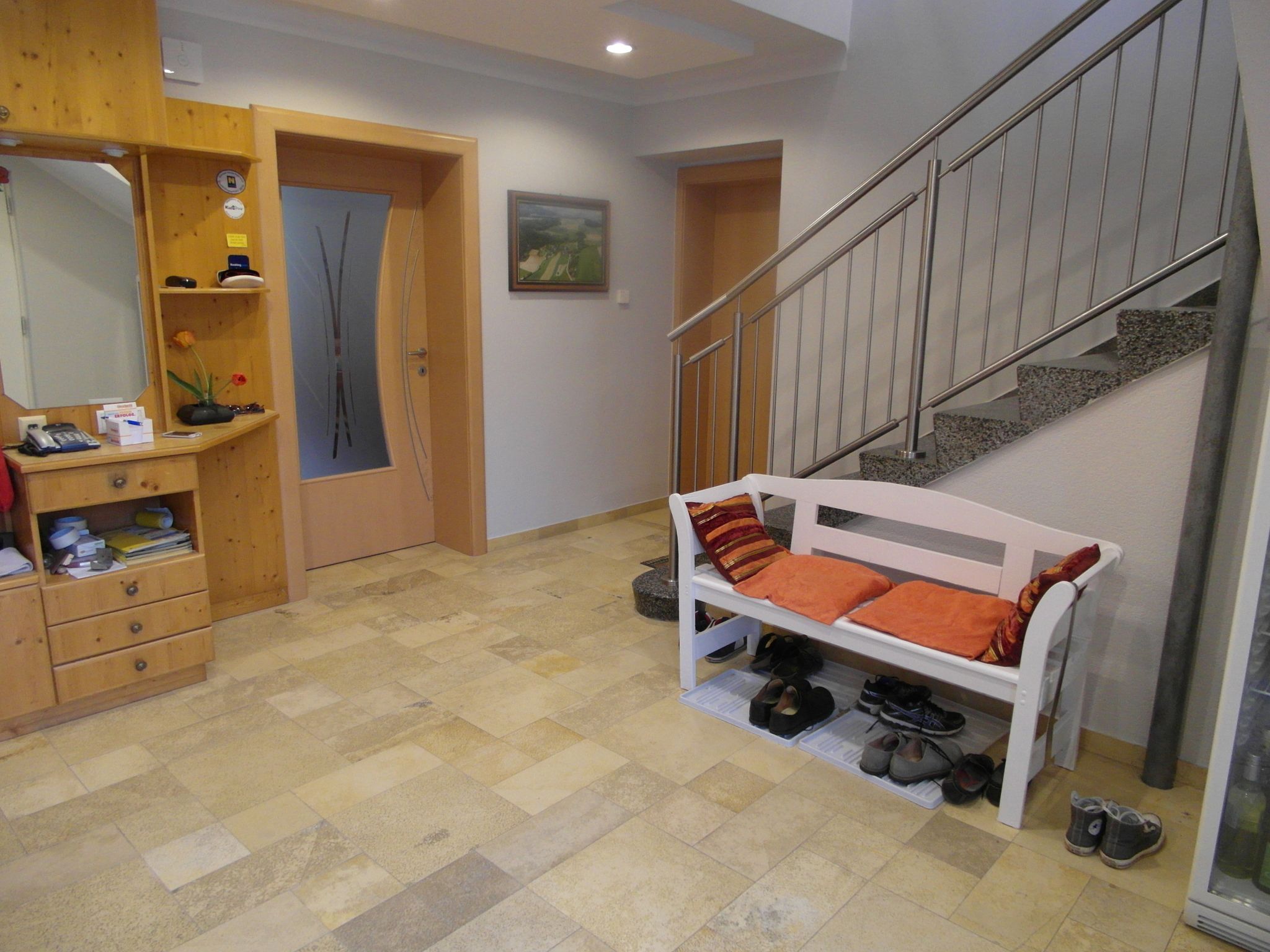 Entrance area with wooden chest of drawers, bench with cushions and stairs.