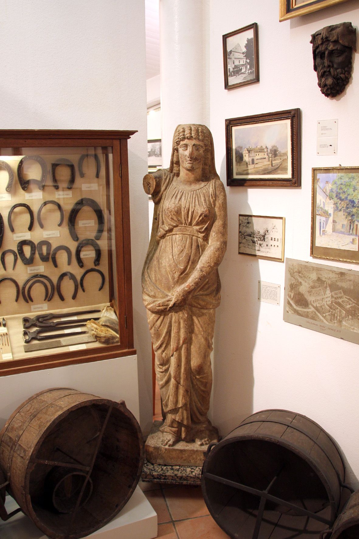 Interior view of a museum with an antique statue, horseshoes in a display case and historical pictures on the wall.
