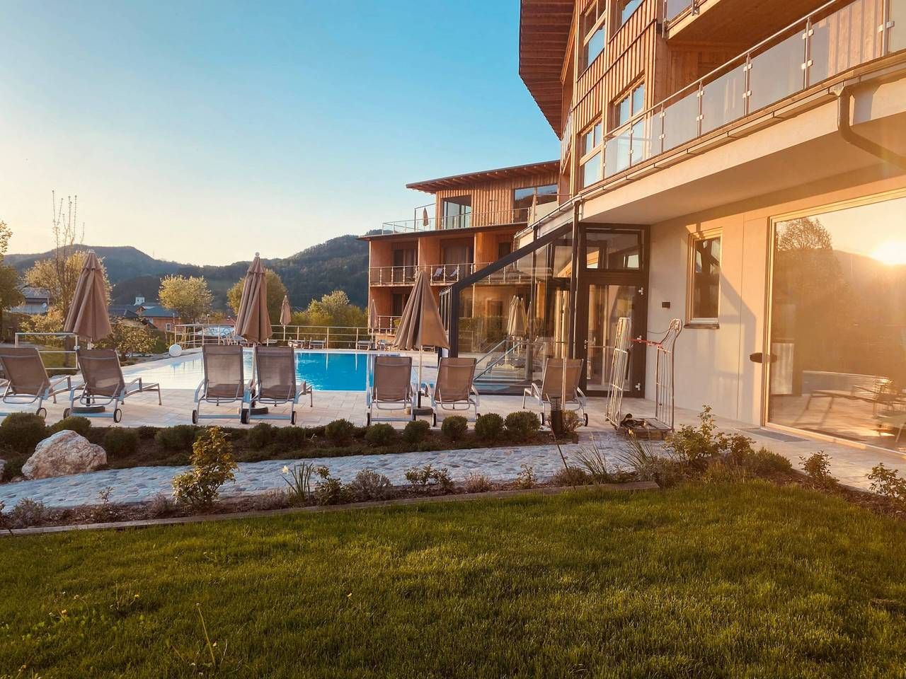 Outdoor area of the Naturhotel Molzbachhof with pool and sun loungers at sunset.
