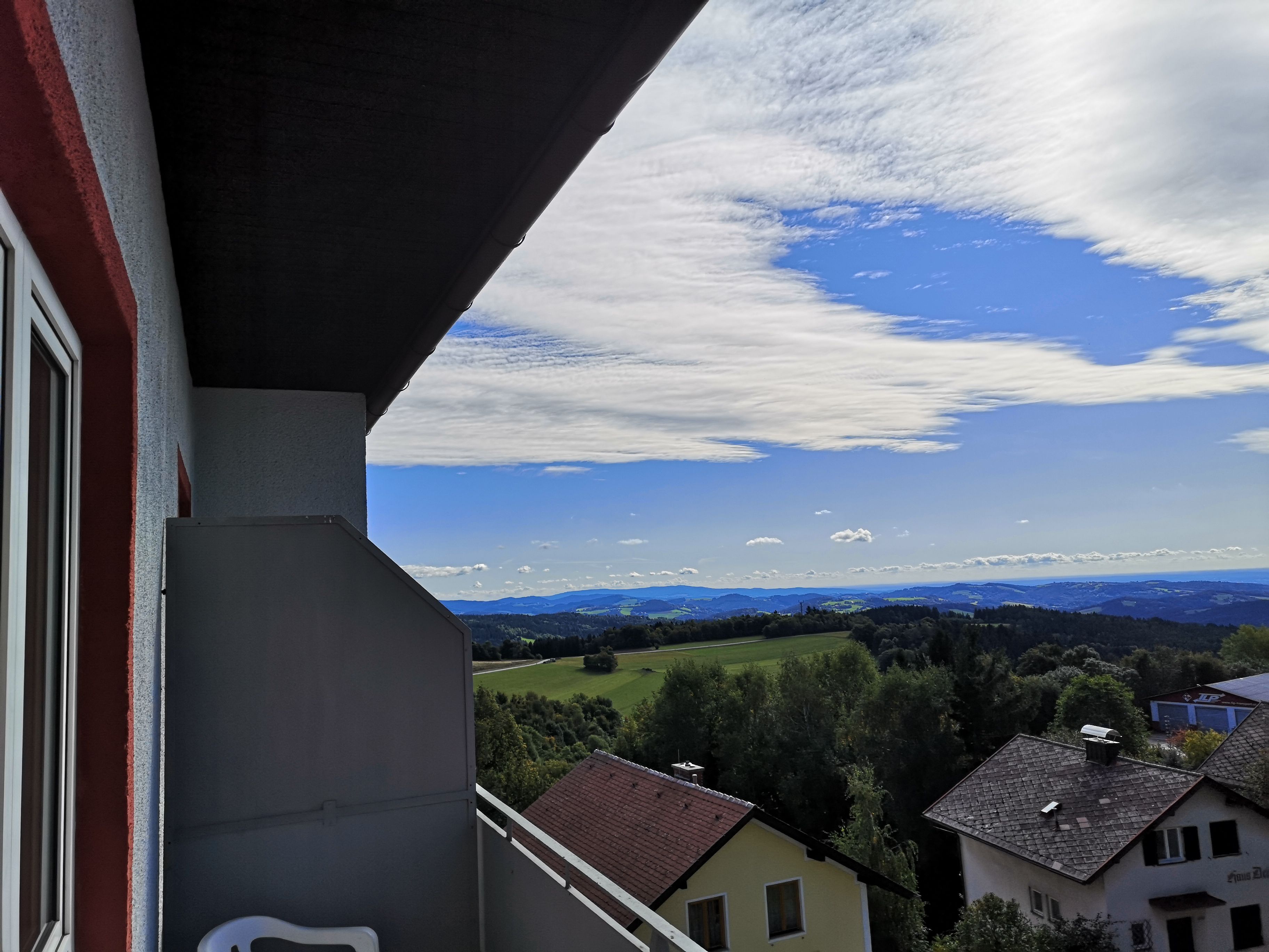 View from a balcony of a landscape with houses, trees and hills under a blue sky with clouds.