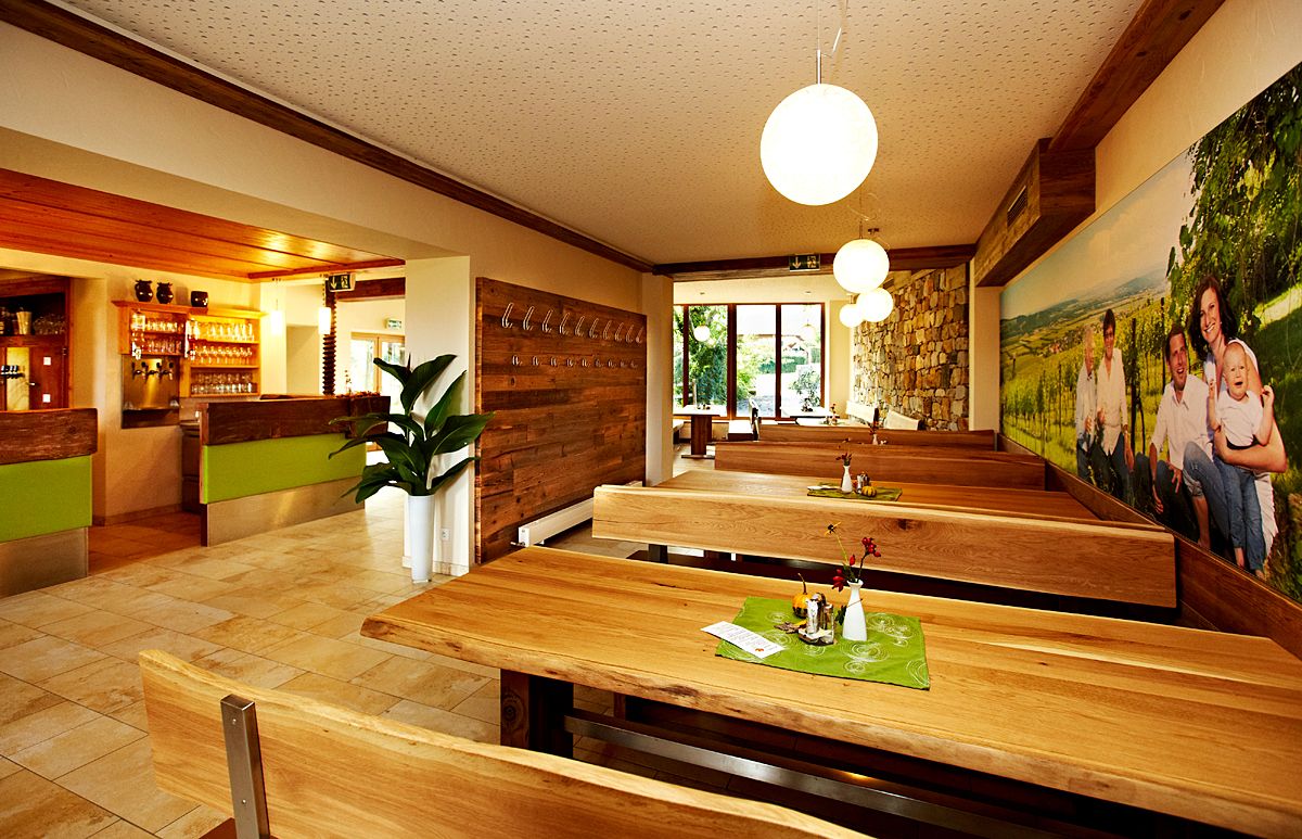 Interior view of a cozy restaurant with wooden tables and benches, decorated with plants and a large mural.