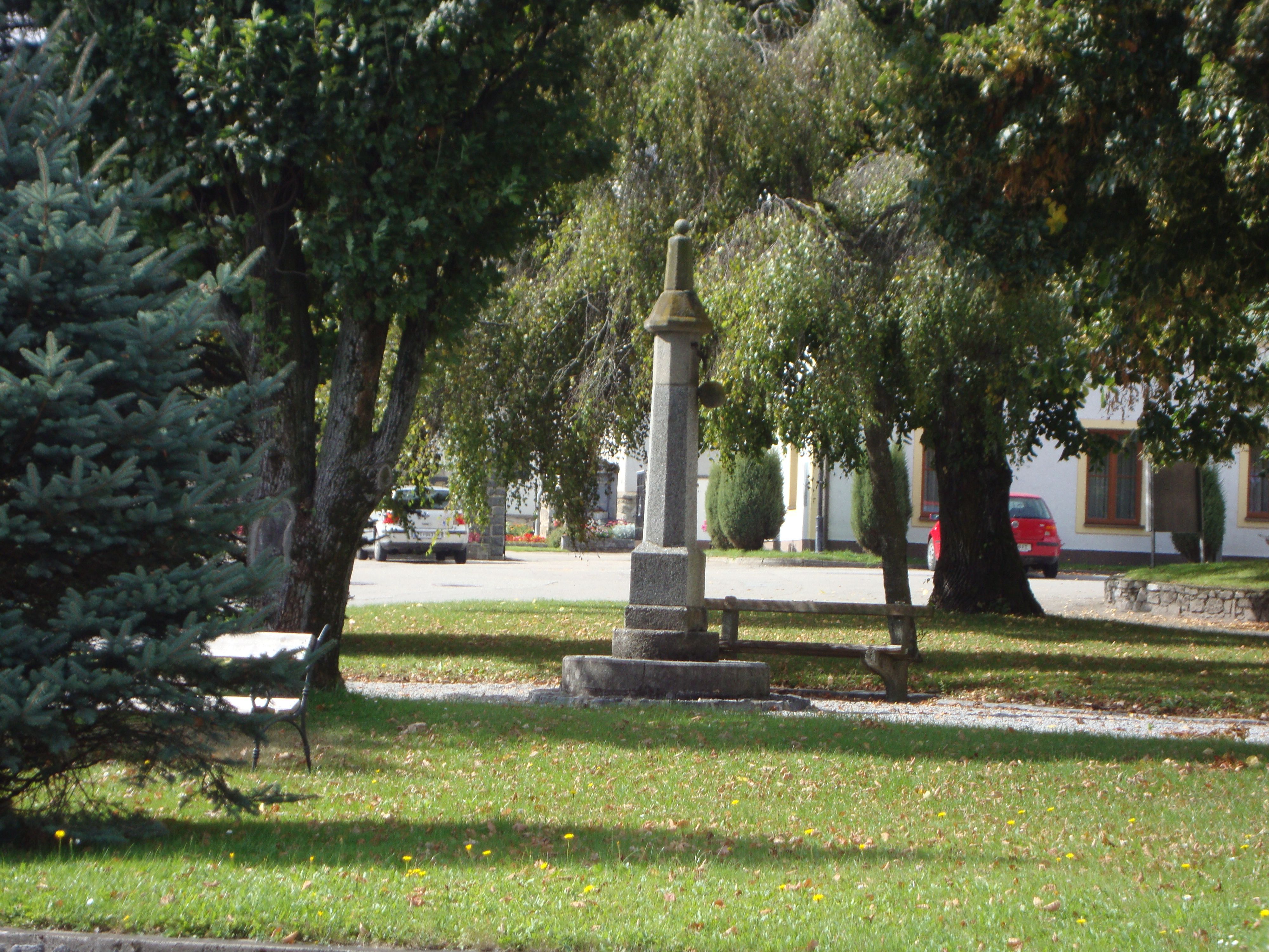 A small park with a stone monument and a bench surrounded by trees.