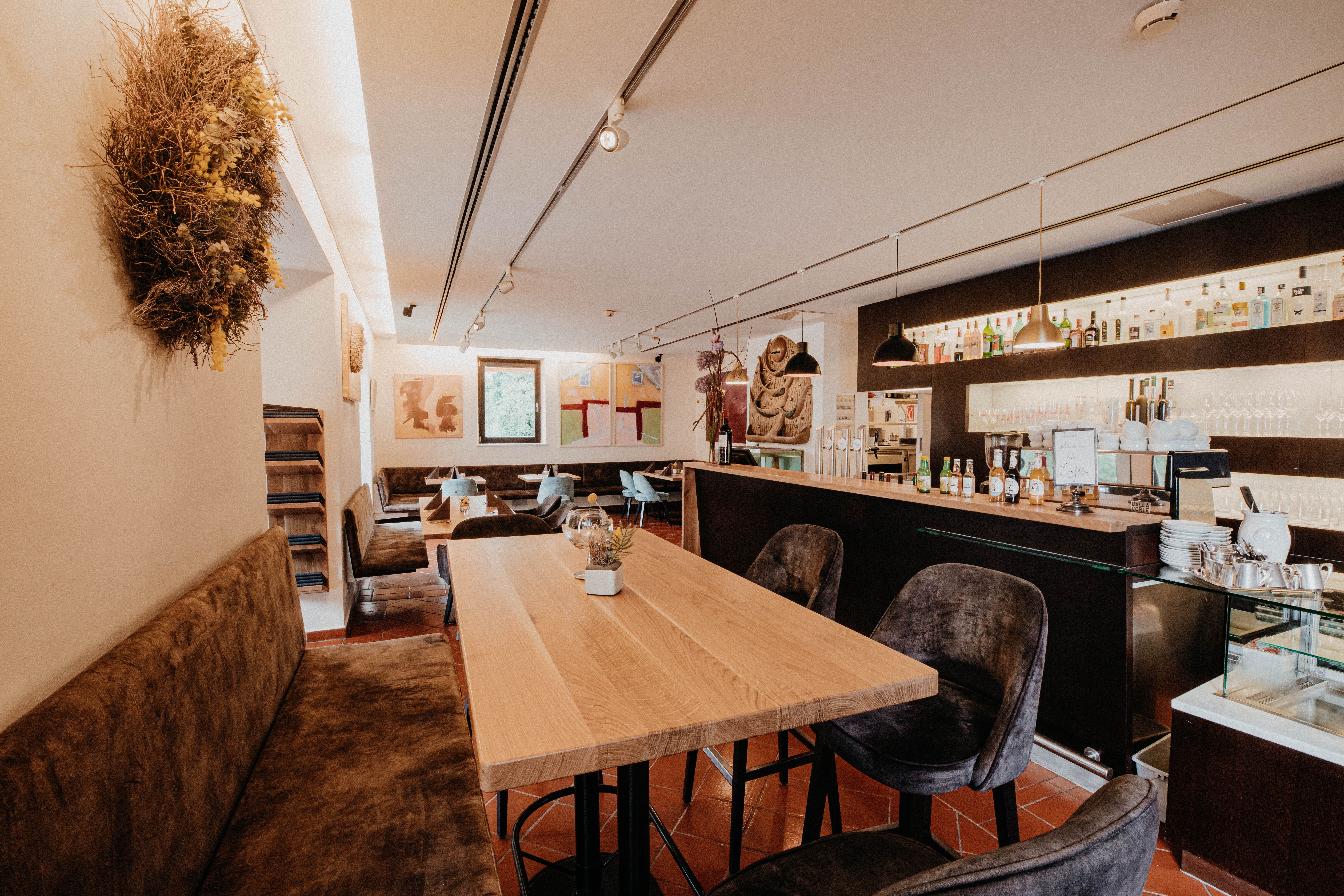 Interior view of a modern restaurant with wooden tables, bar and works of art on the walls.