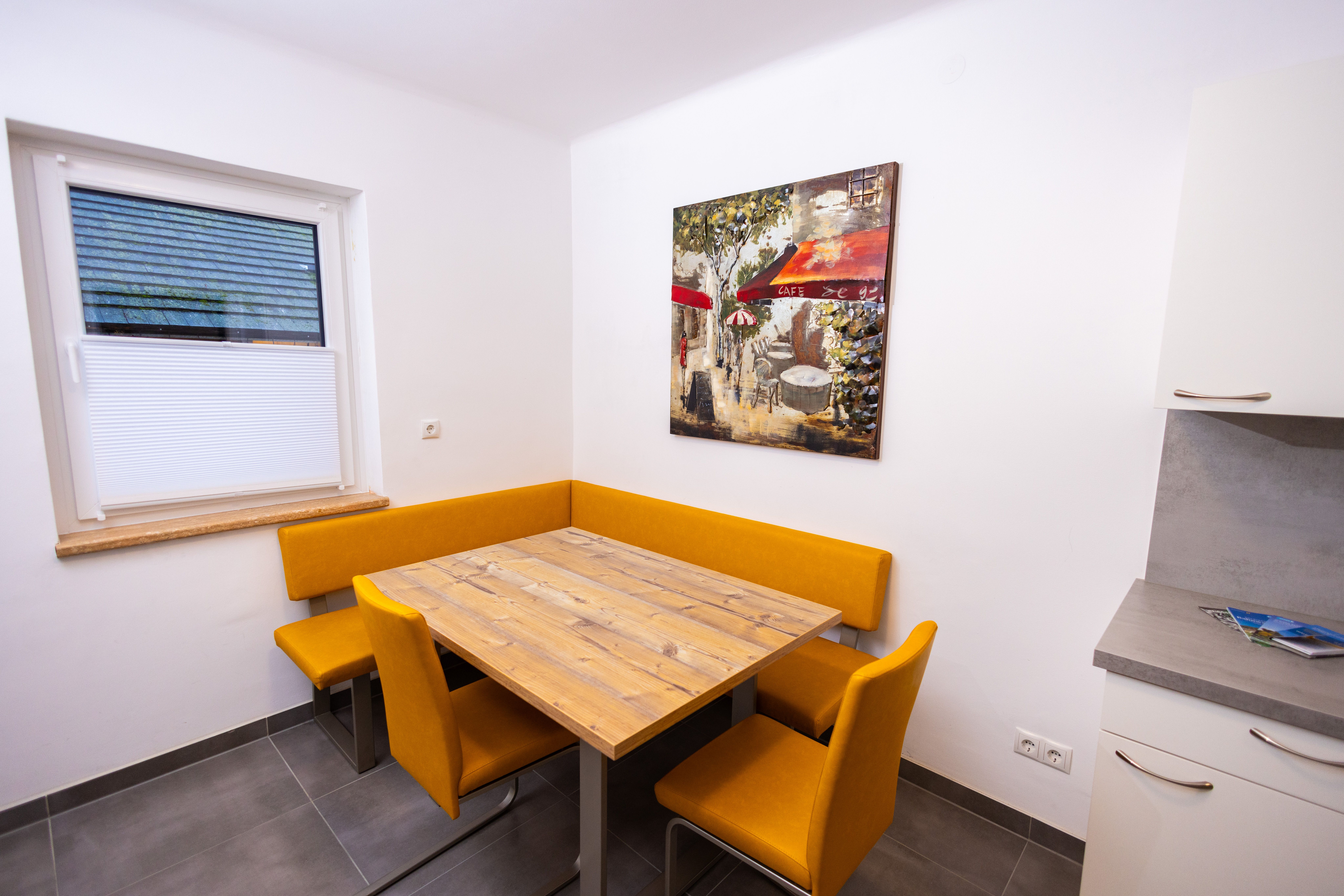 Dining area with wooden table, yellow chairs and mural of a café.