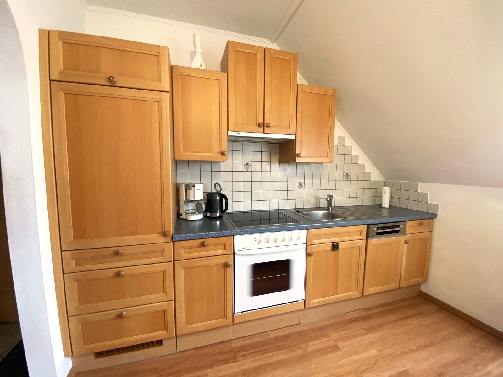 Kitchen unit with wooden cupboards, stove, sink and tiled splashback.