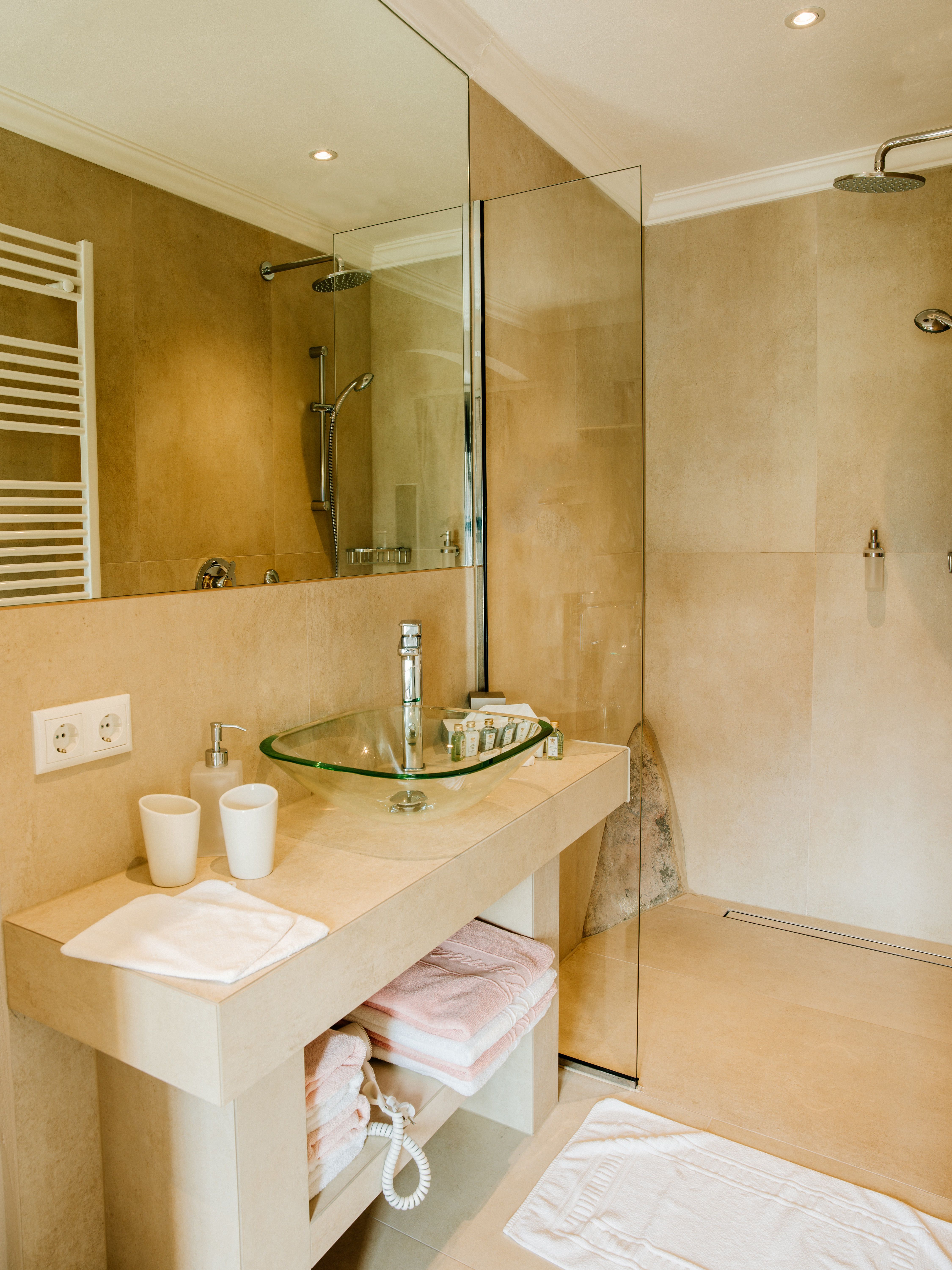Modern bathroom with glass washbasin and walk-in shower.