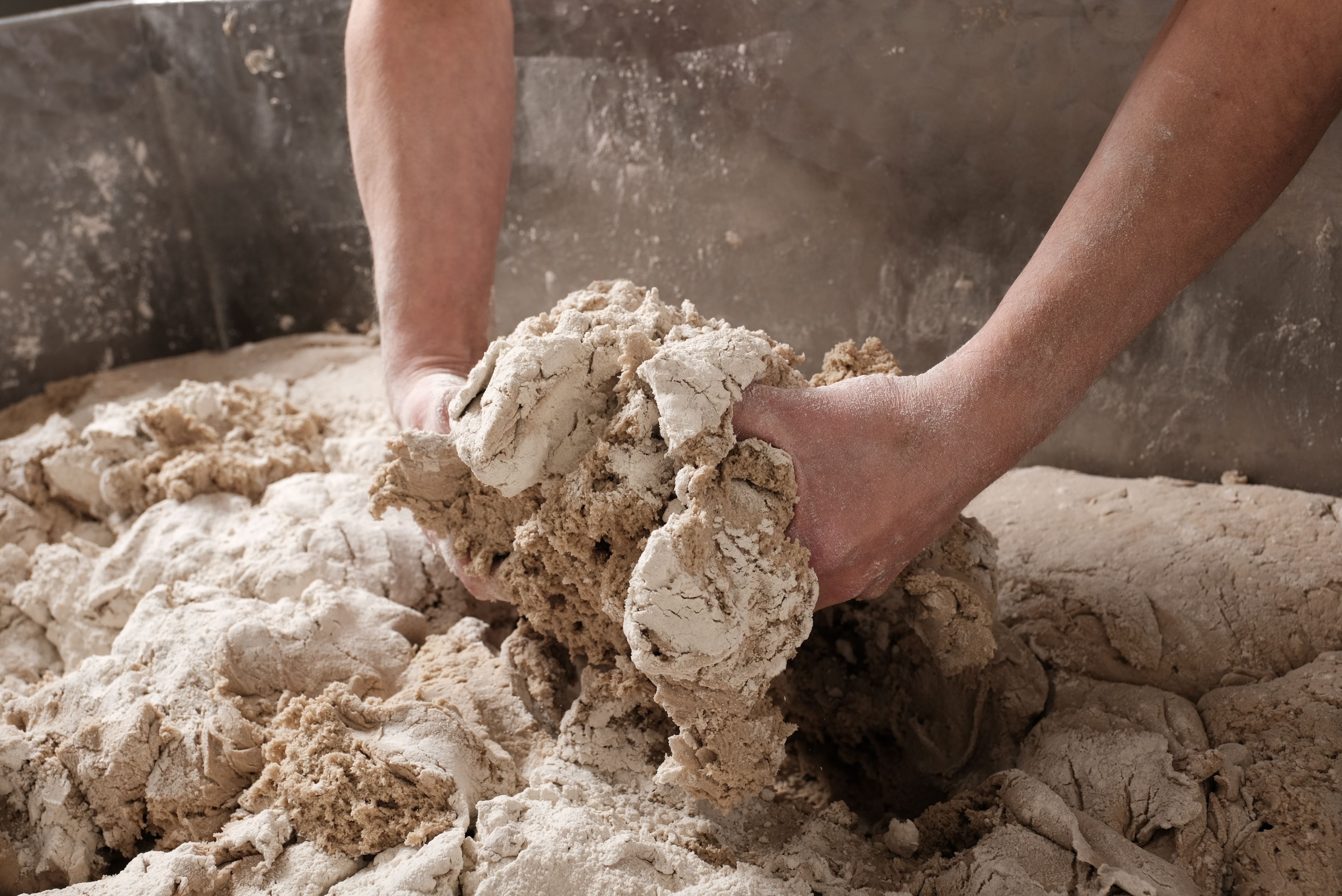 Hands knead dough in a large bowl.