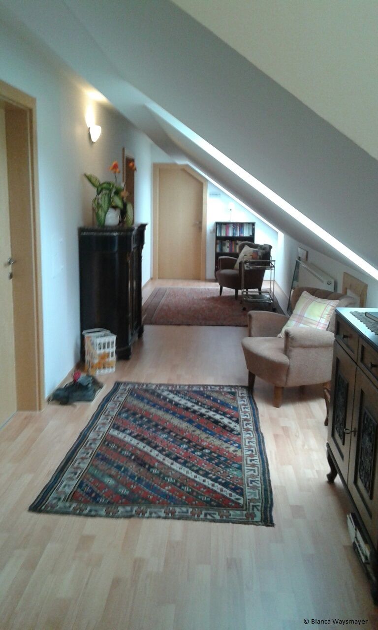 A cozy attic hallway with carpet, plants and furniture.