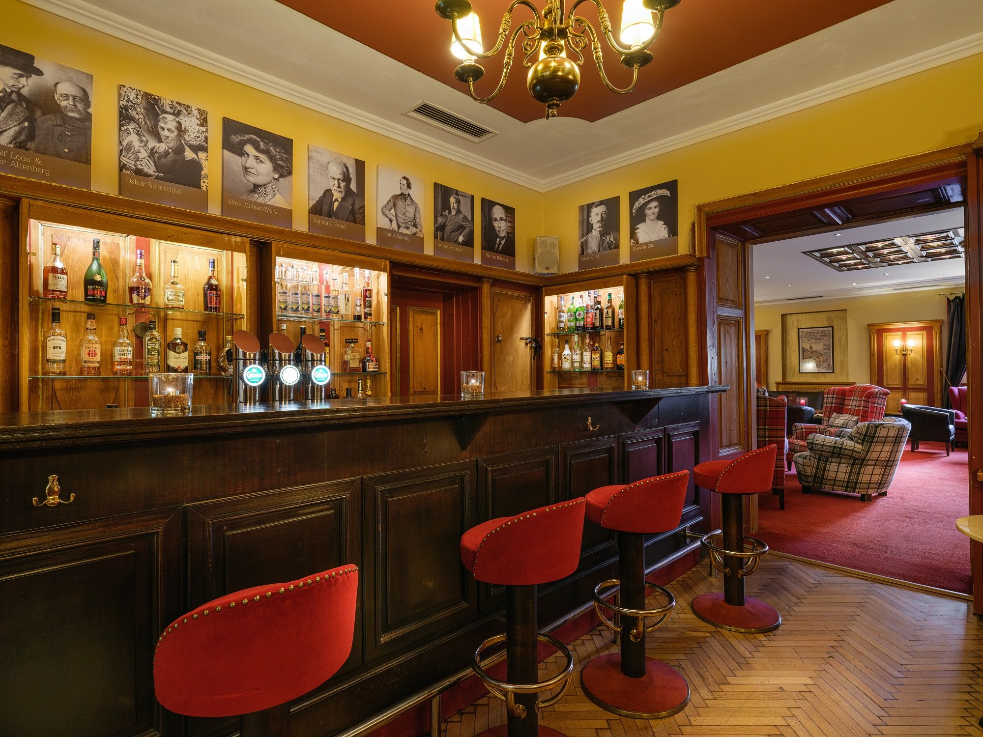 Interior view of a stylish bar with wooden counter, red bar stools and pictures on the wall.