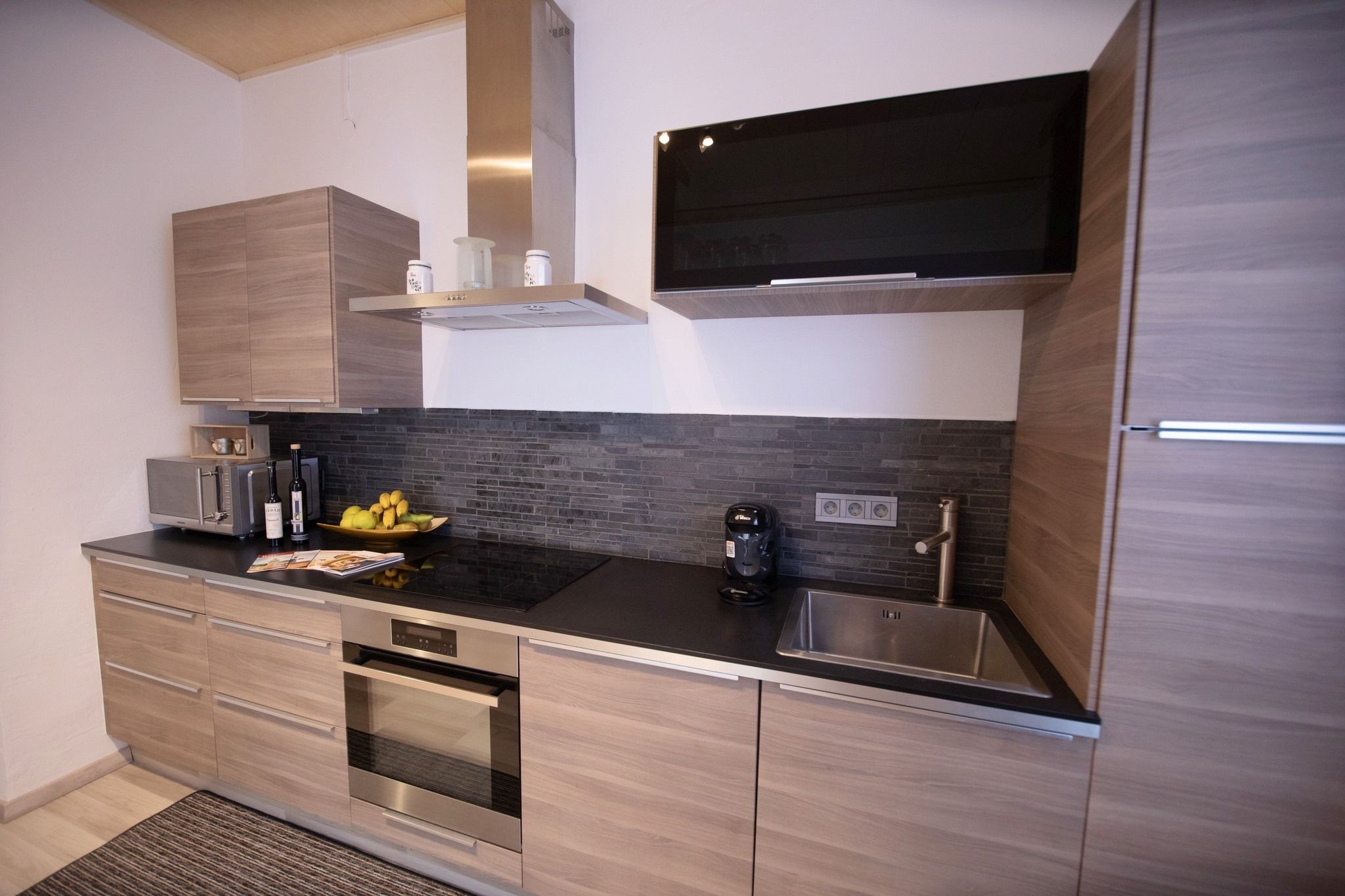 Modern kitchen with wooden cupboards, black worktop, sink, stove and extractor hood.