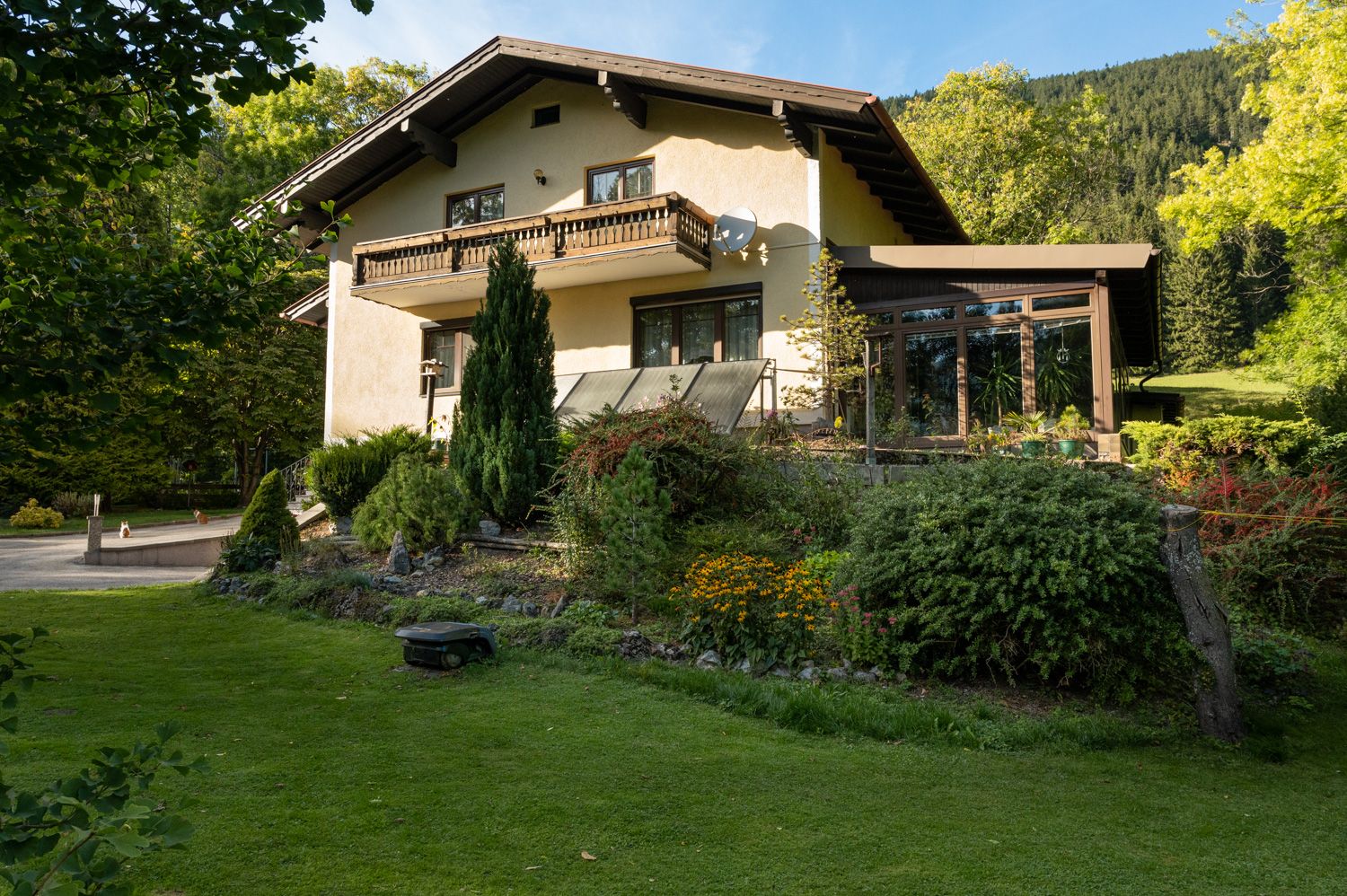 A two-storey vacation home with balcony and garden, surrounded by trees and meadow.