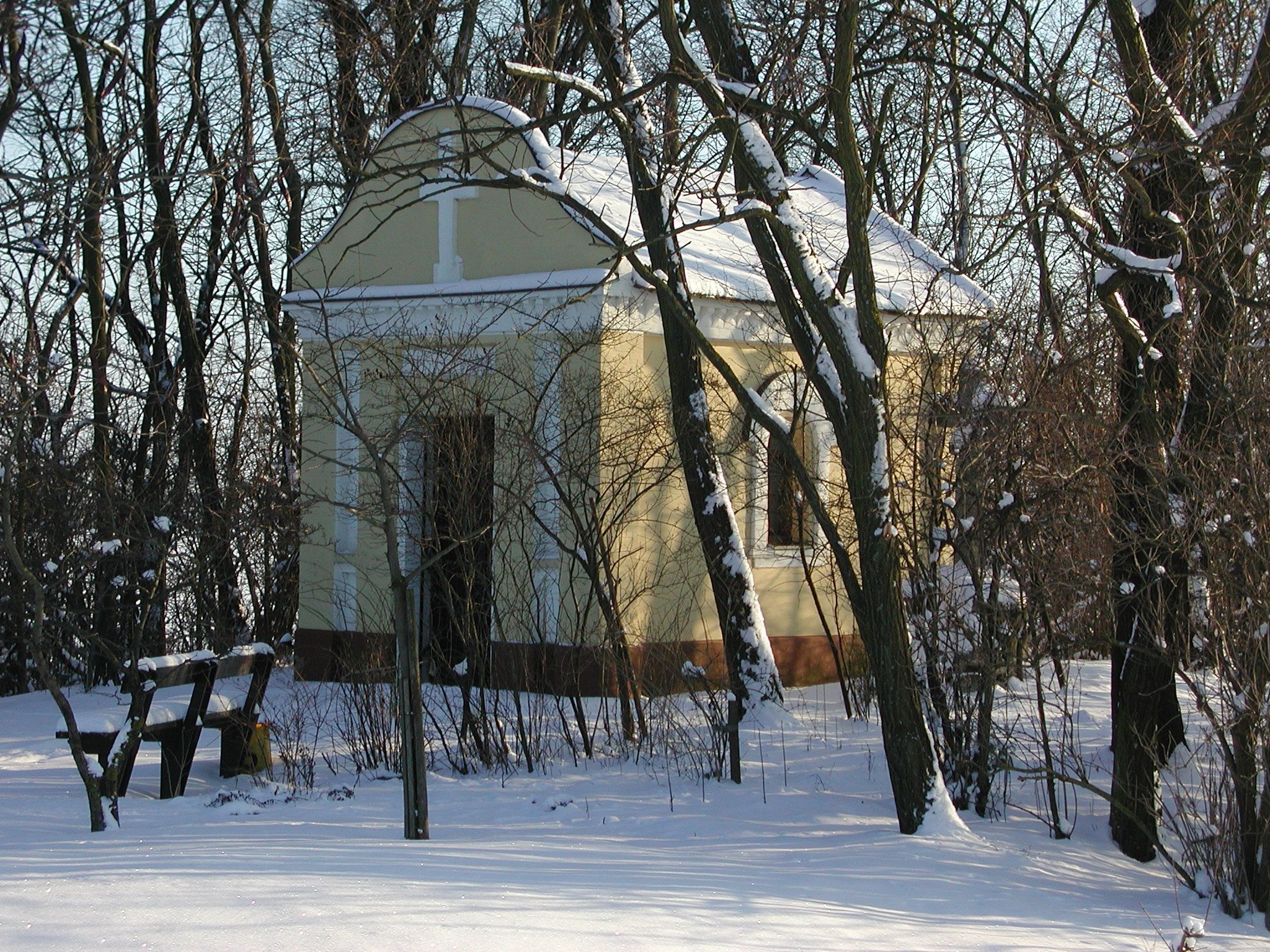 A small chapel in winter, surrounded by snow-covered trees.