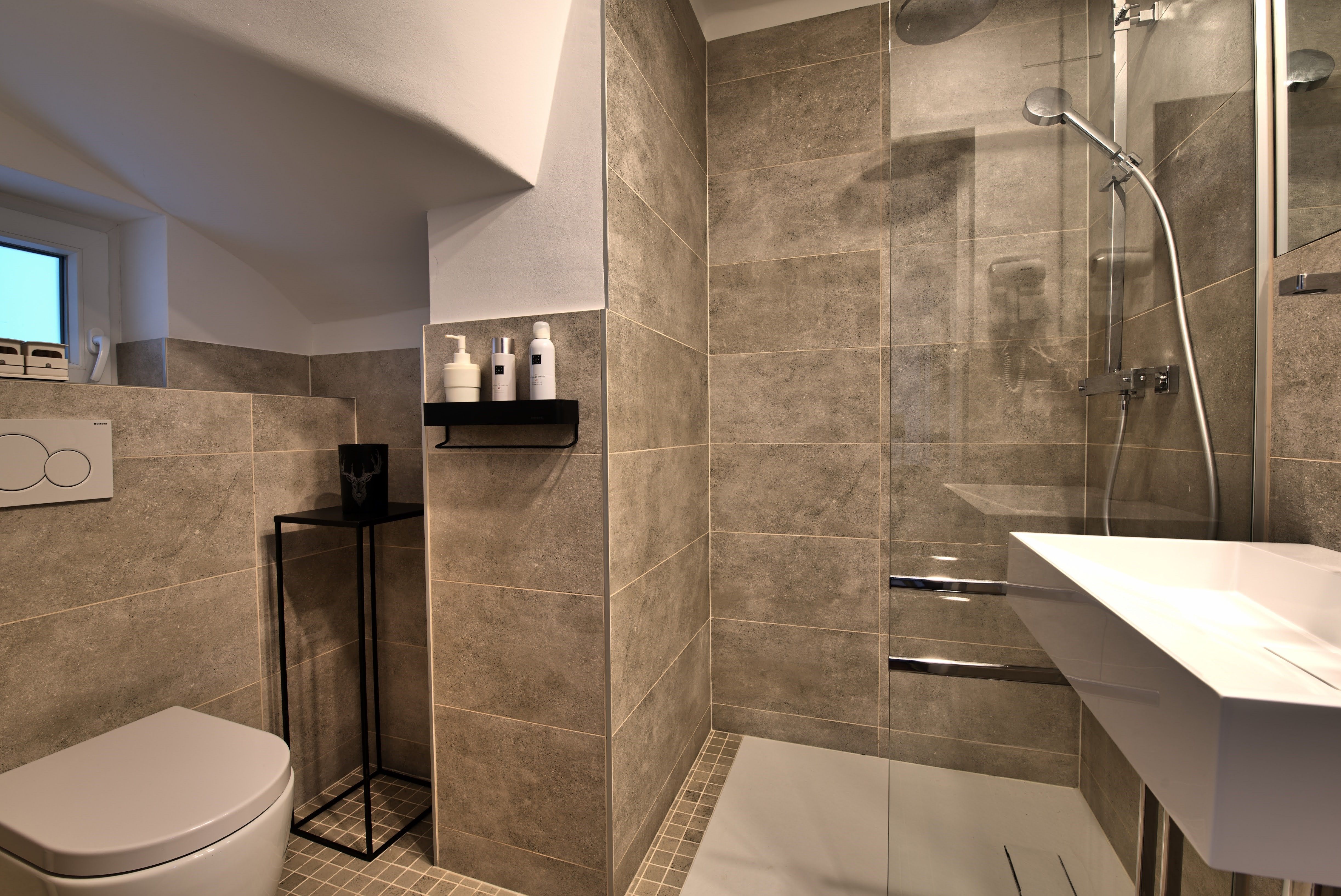 Modern bathroom with gray tiles, shower, washbasin and toilet.