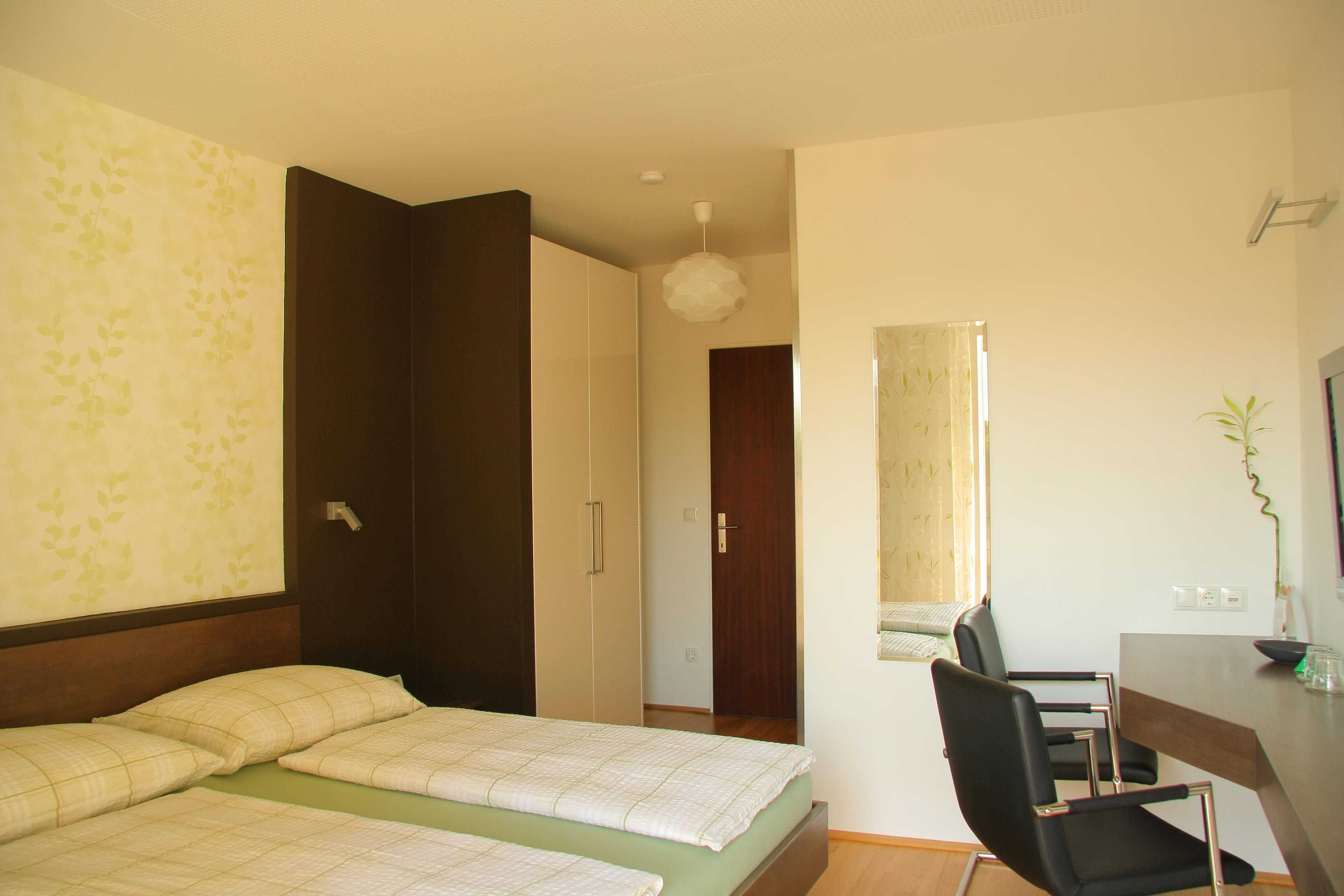 A modern hotel room with two single beds, a desk and a chair. The walls are bright and decorated with a plant pattern.
