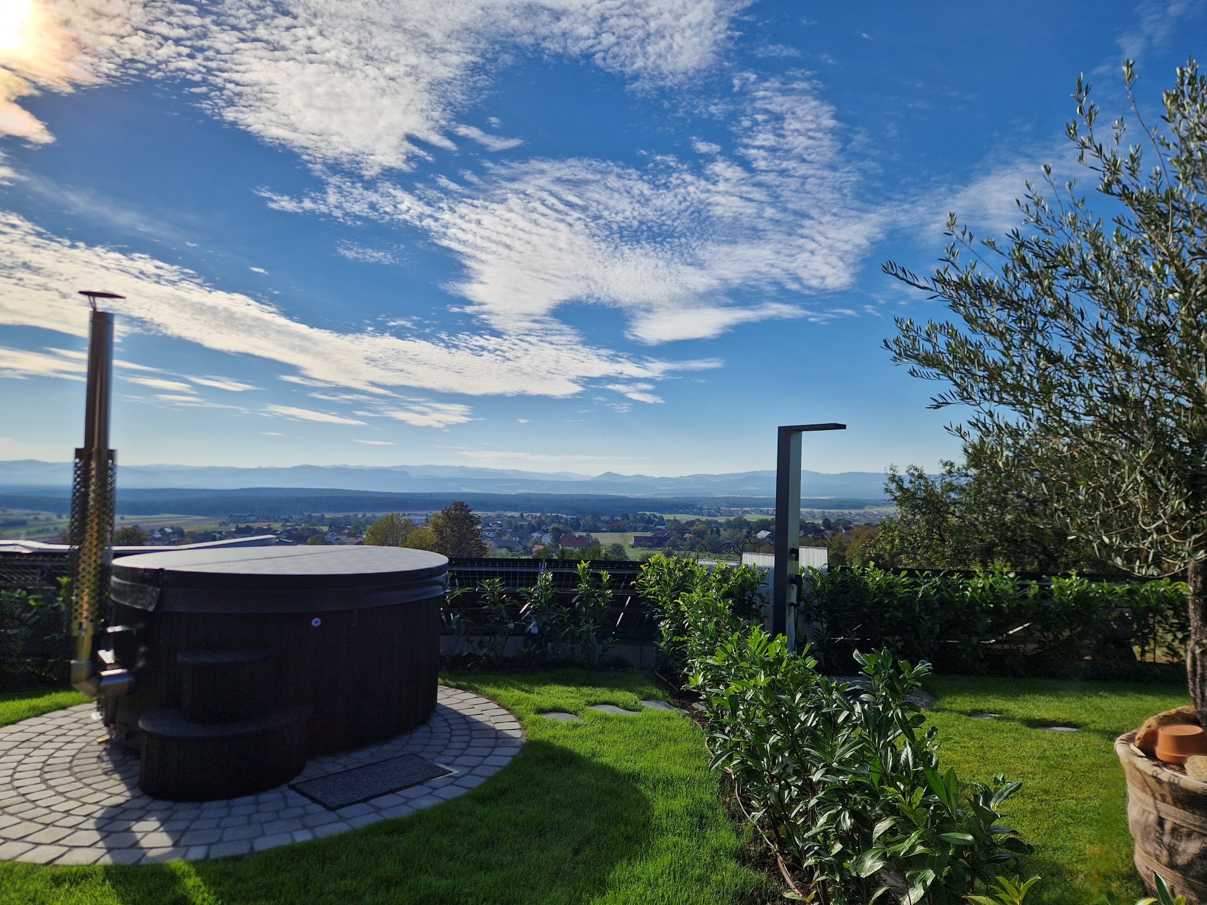 A round whirlpool in the garden with a view of a vast landscape and blue sky.