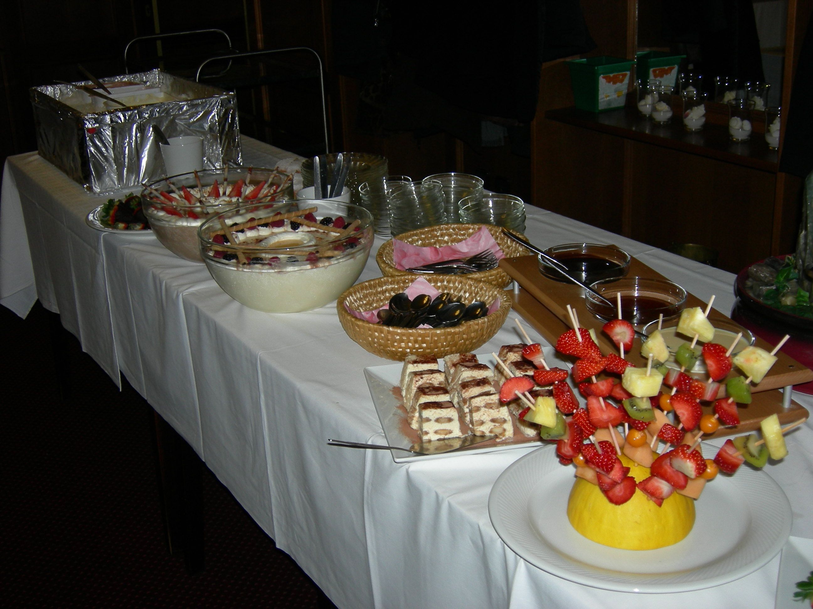 Buffet with desserts and fruit skewers on a table.