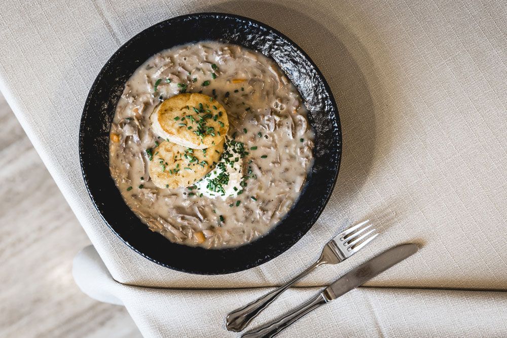 A plate with Beuschl and two bread dumplings, garnished with chives, on a table with cutlery.