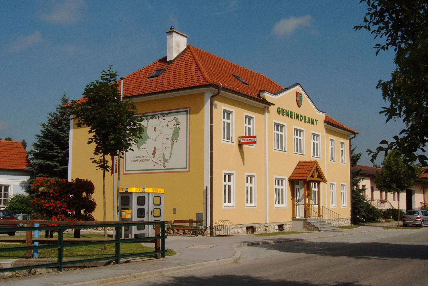 A yellow building with the inscription 'Gemeindeamt', a coat of arms and a map on the wall.