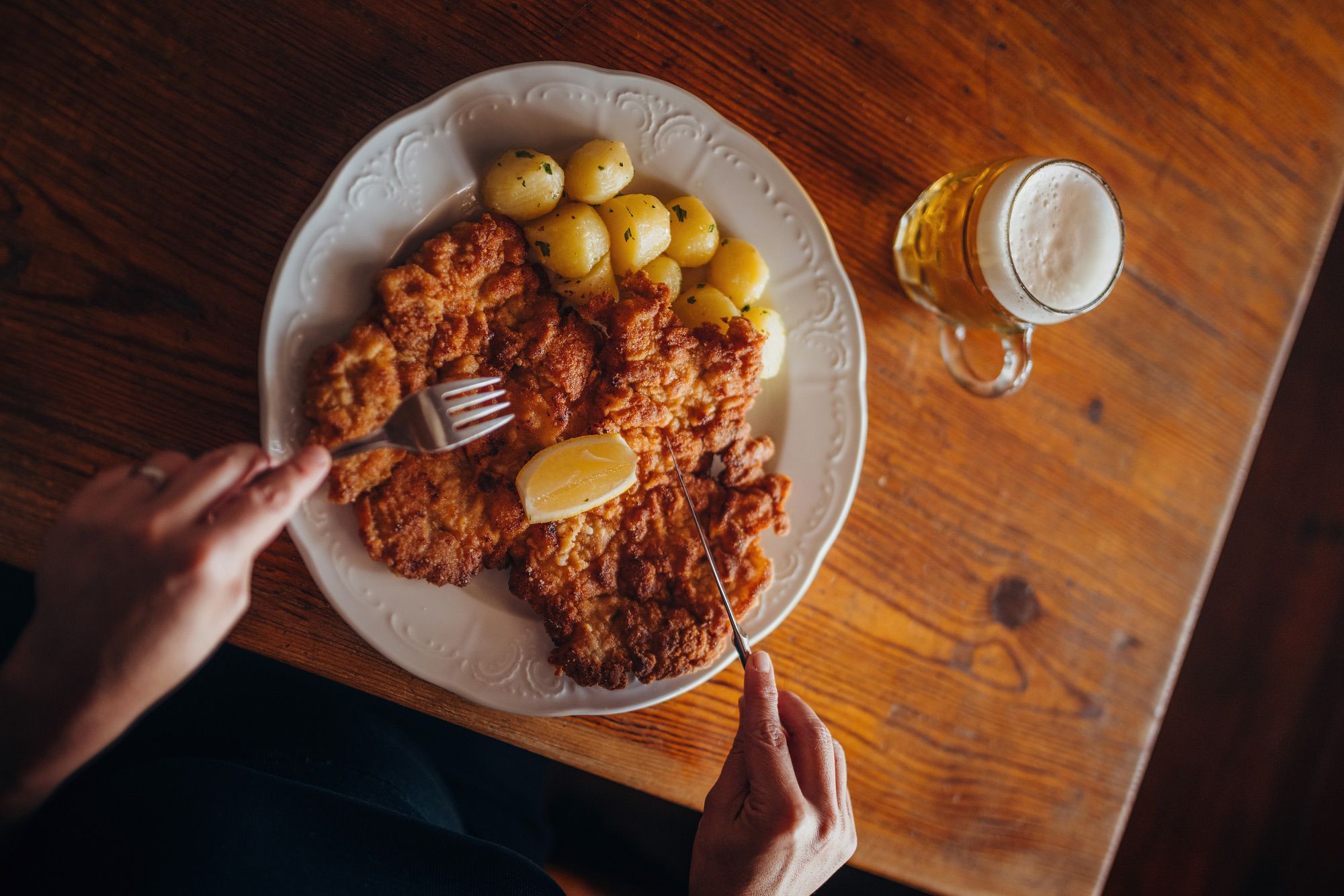 Plate with schnitzel, potatoes and lemon, next to a glass of beer.