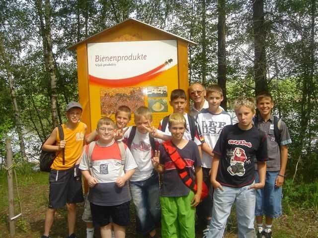 Group of boys in front of a sign with the inscription 'Bee products' outdoors.